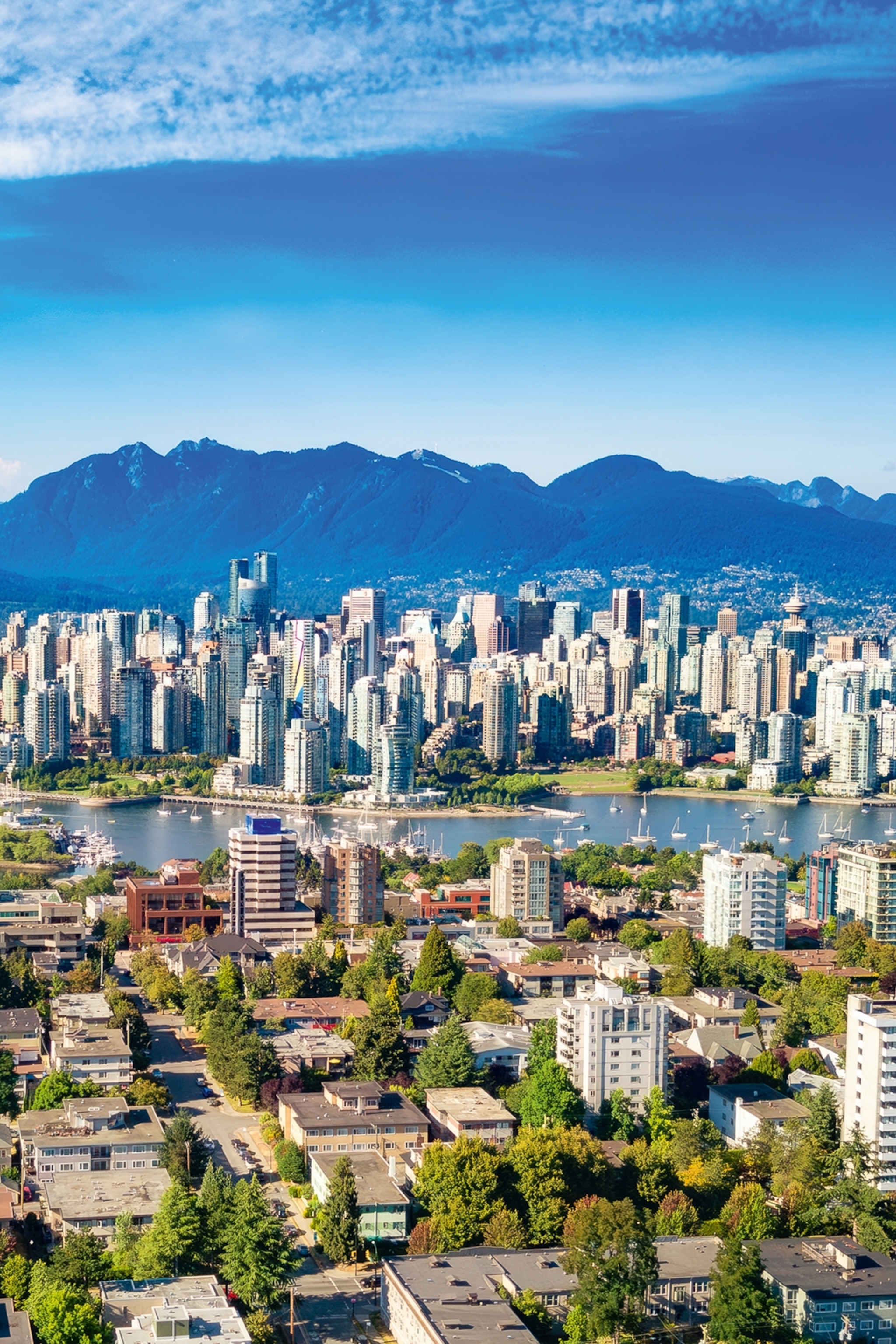 A city skyline with high-rising buildings, a river running through the center and a mountain range in the background.
