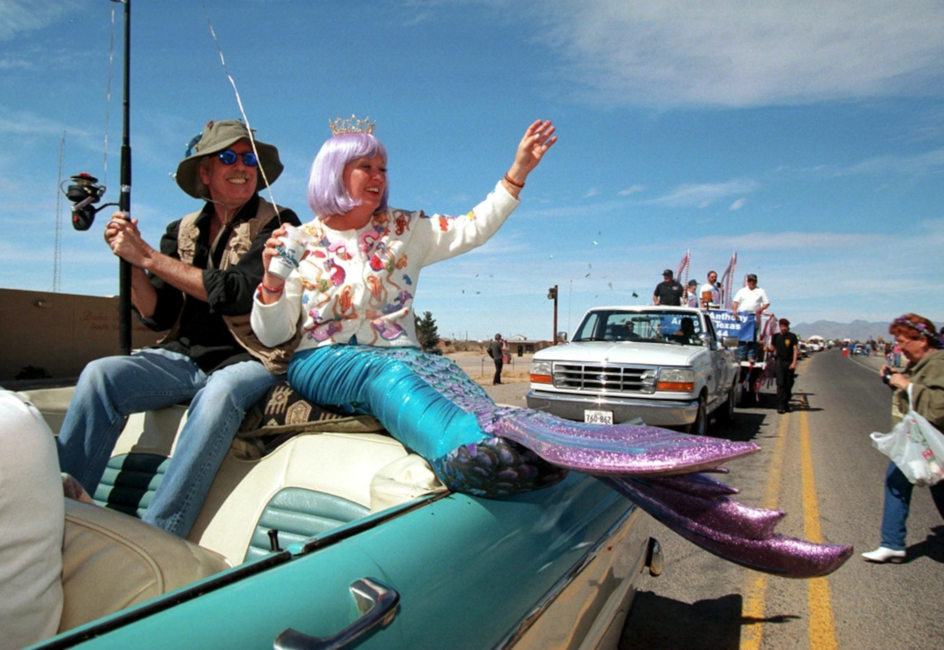 Cars filled with waving people drive in a leap year parade in Anthony, New Mexico.