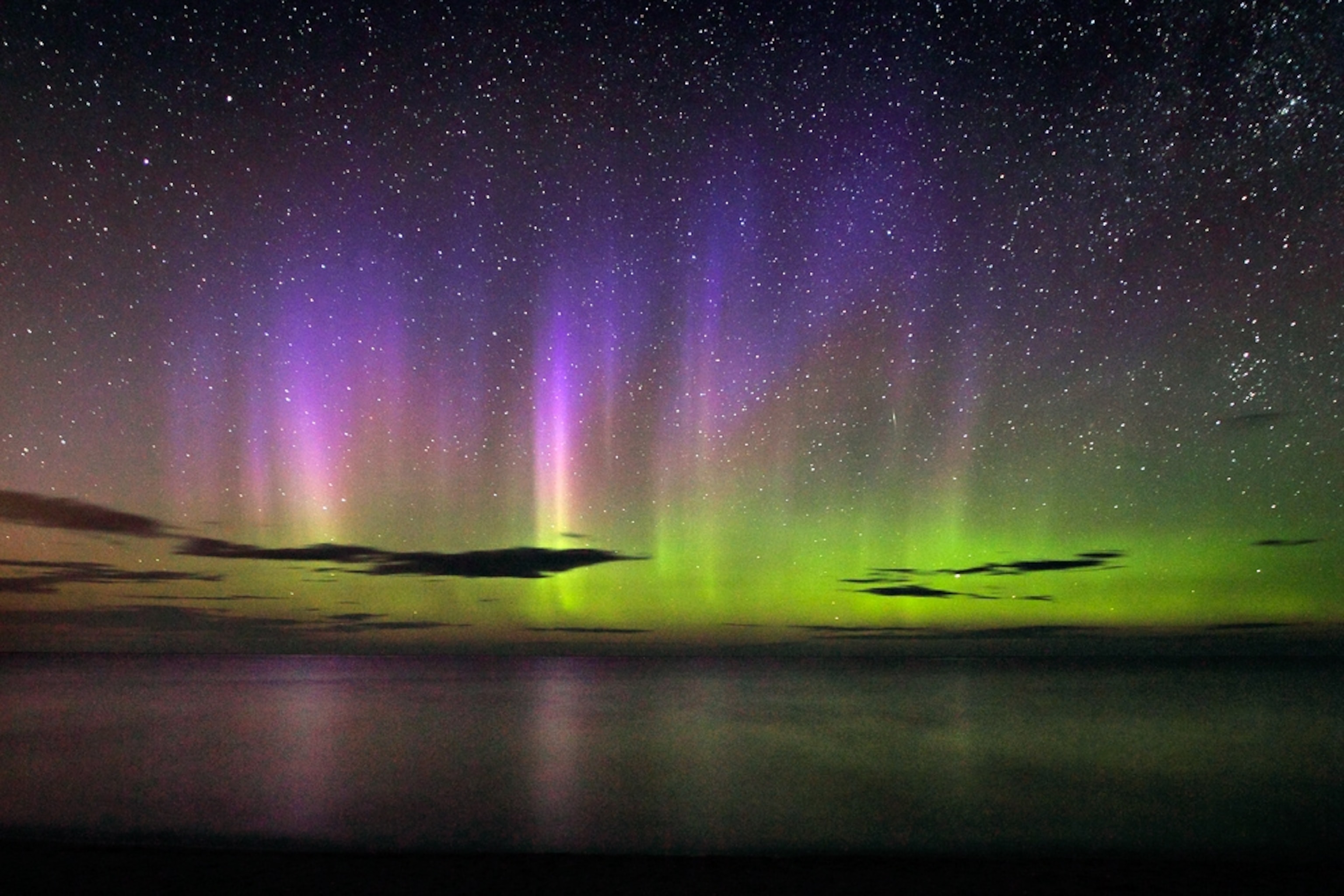 Picture of a green aurora topped by purple rays over Lake Superior.