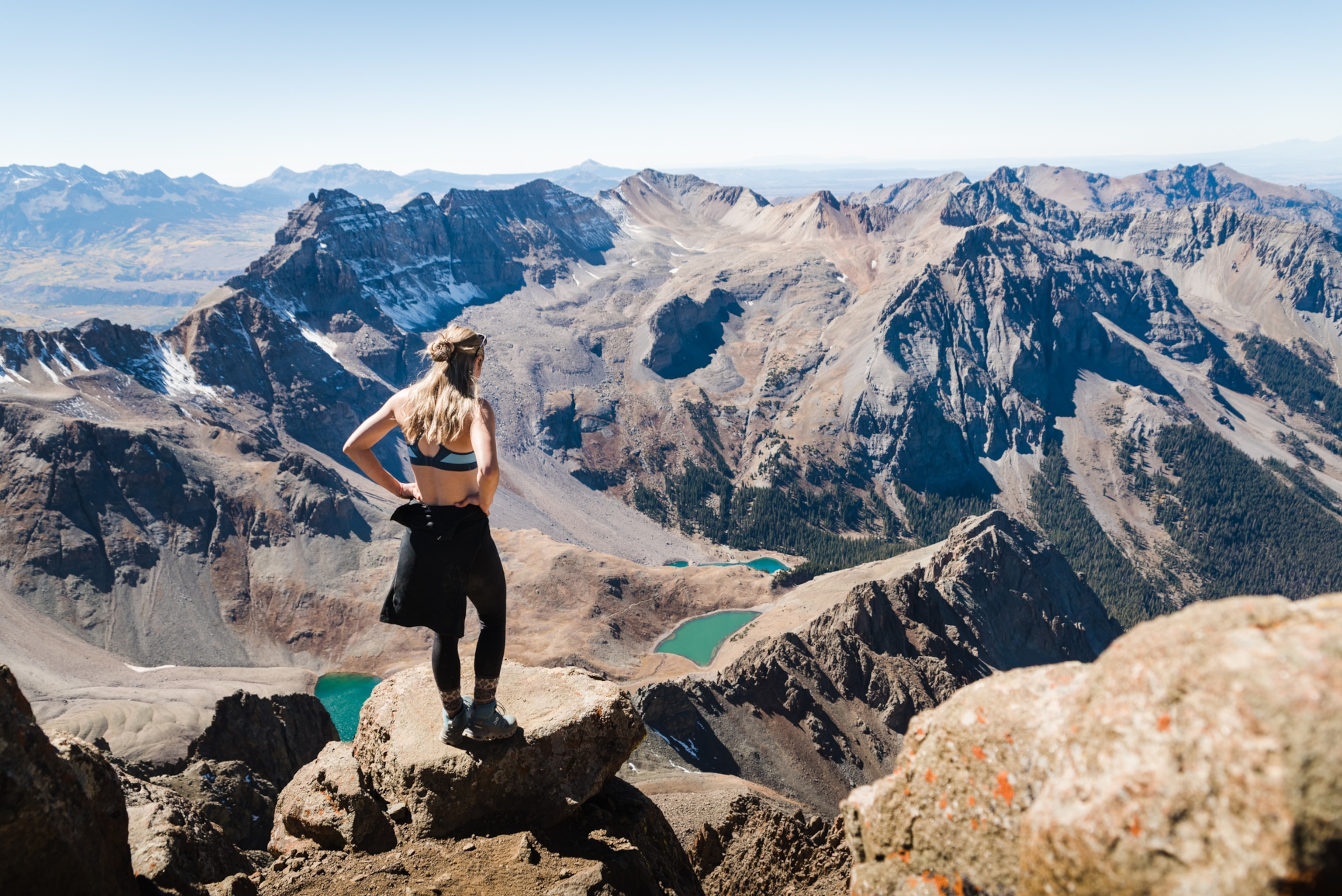 A woman standing at the summit of Mount Sneffles enjoying the view of the Blue Lakes.