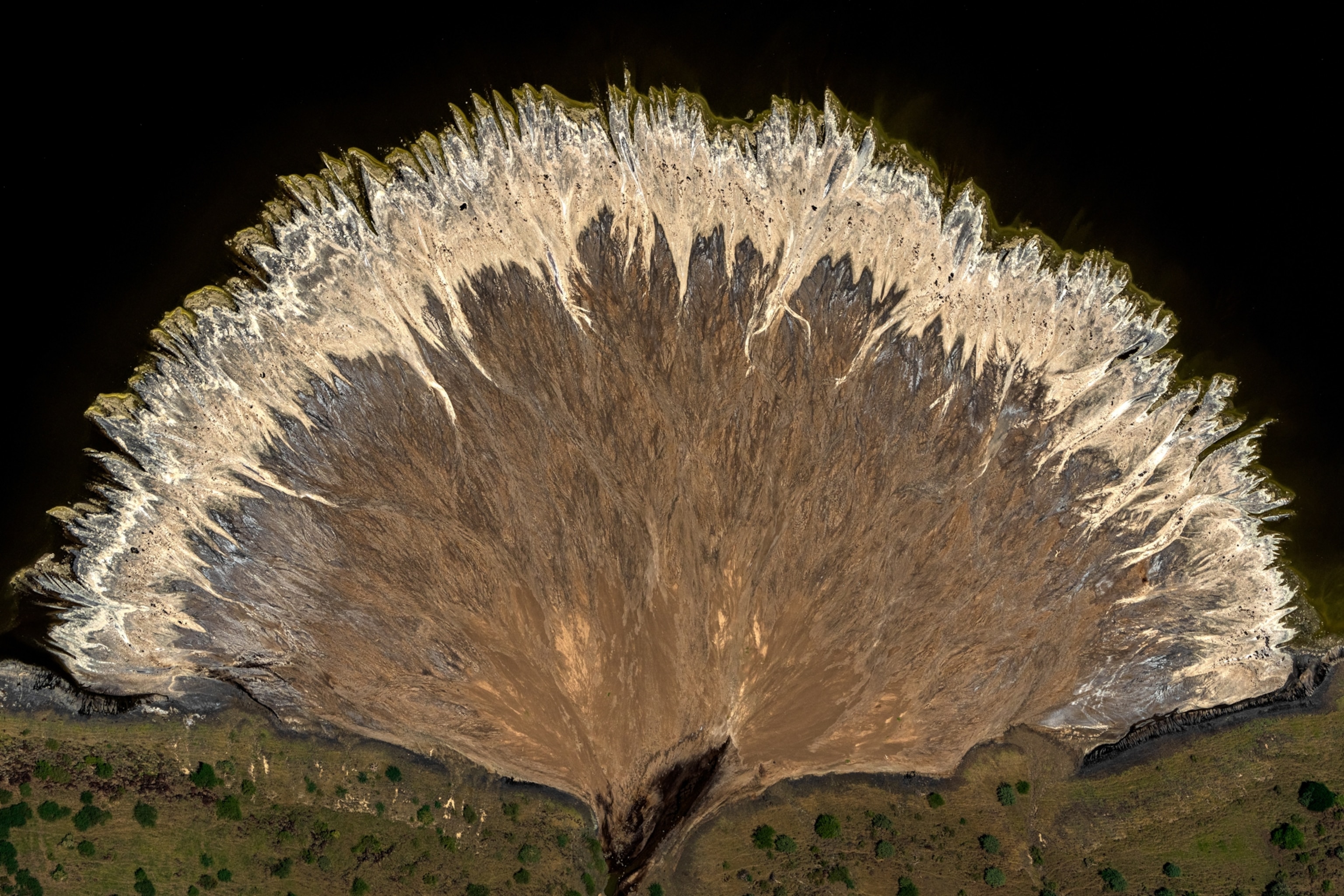 Aerial view of a large, fan-shaped sand formation with intricate patterns, bordered by dark water.