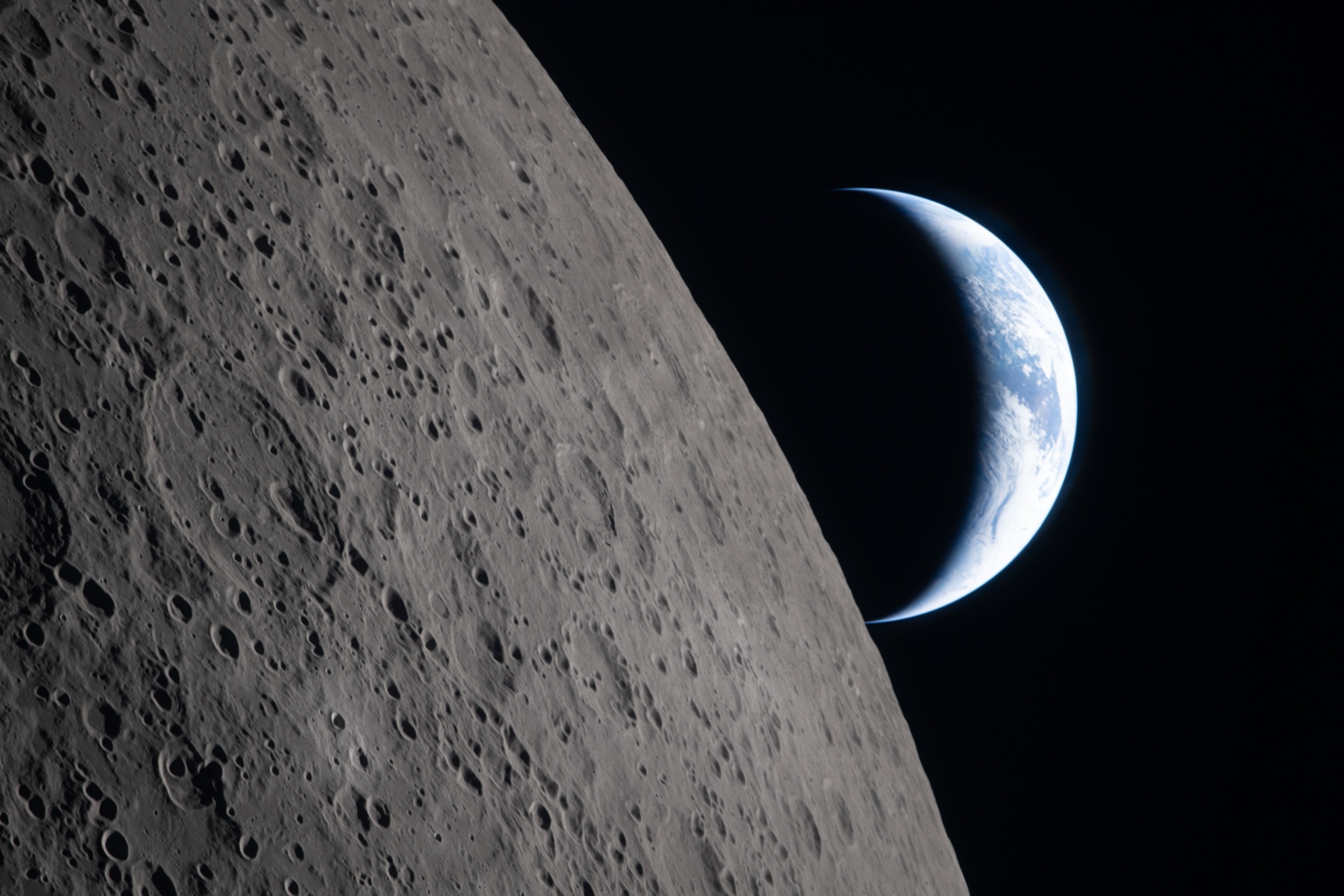 A rugged, cratered lunar surface in the foreground with a crescent Earth glowing against the blackness of space