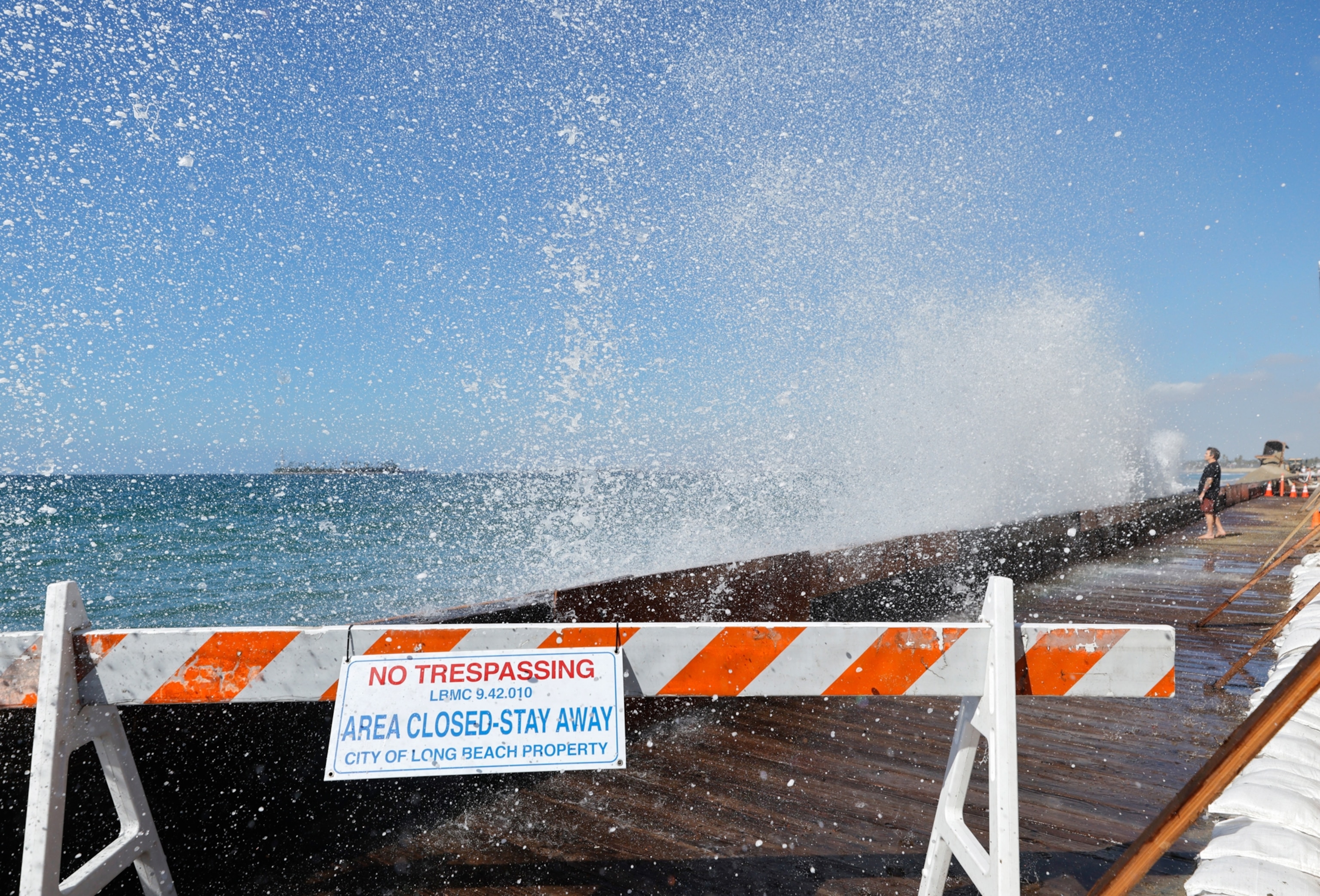 A person watches on a closed section of boardwalk as a Pacific Ocean wave crashes into a seawall protecting beachfront homes on September 28, 2026 in Long Beach, California.