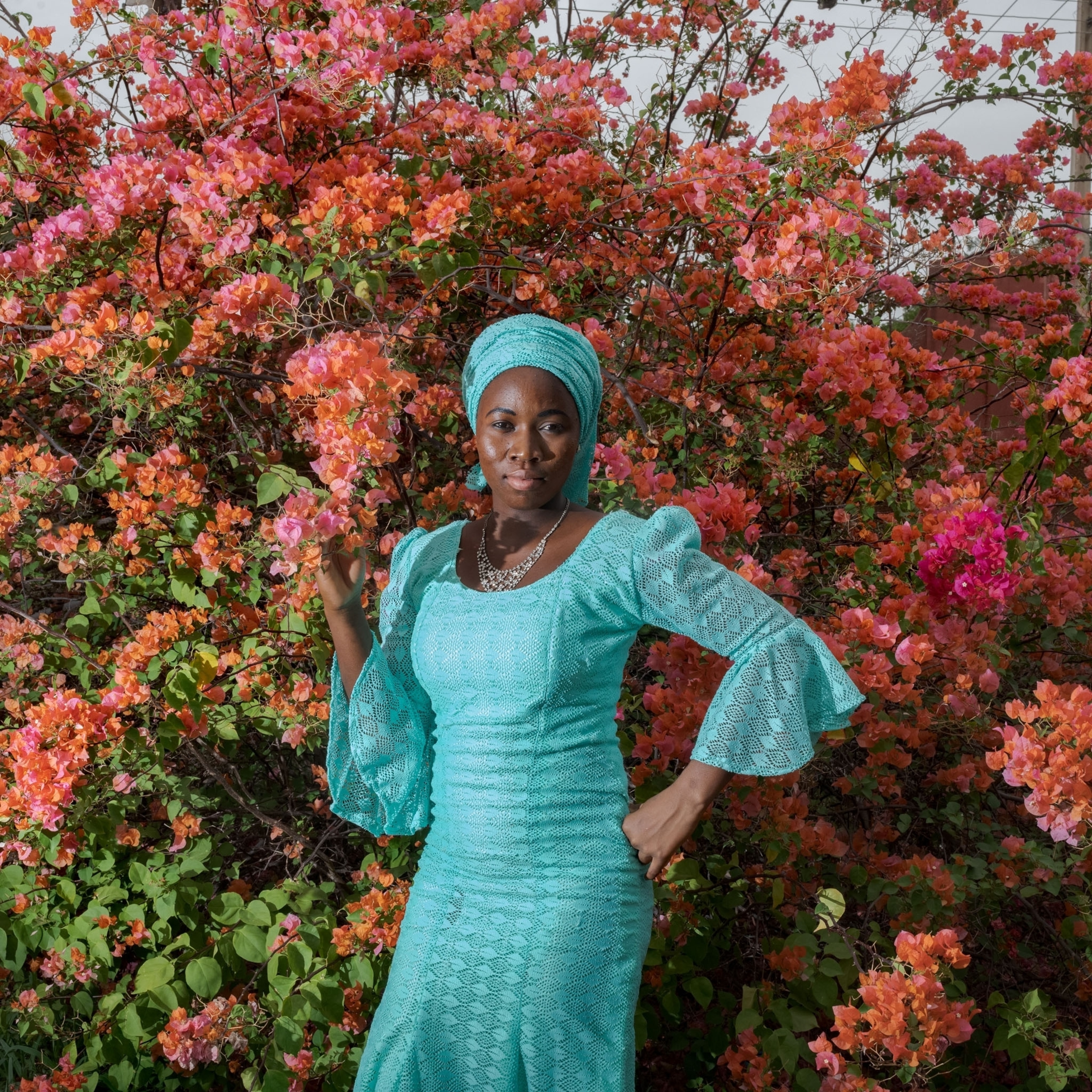 a woman a teal dress standing in front a pink flower bush
