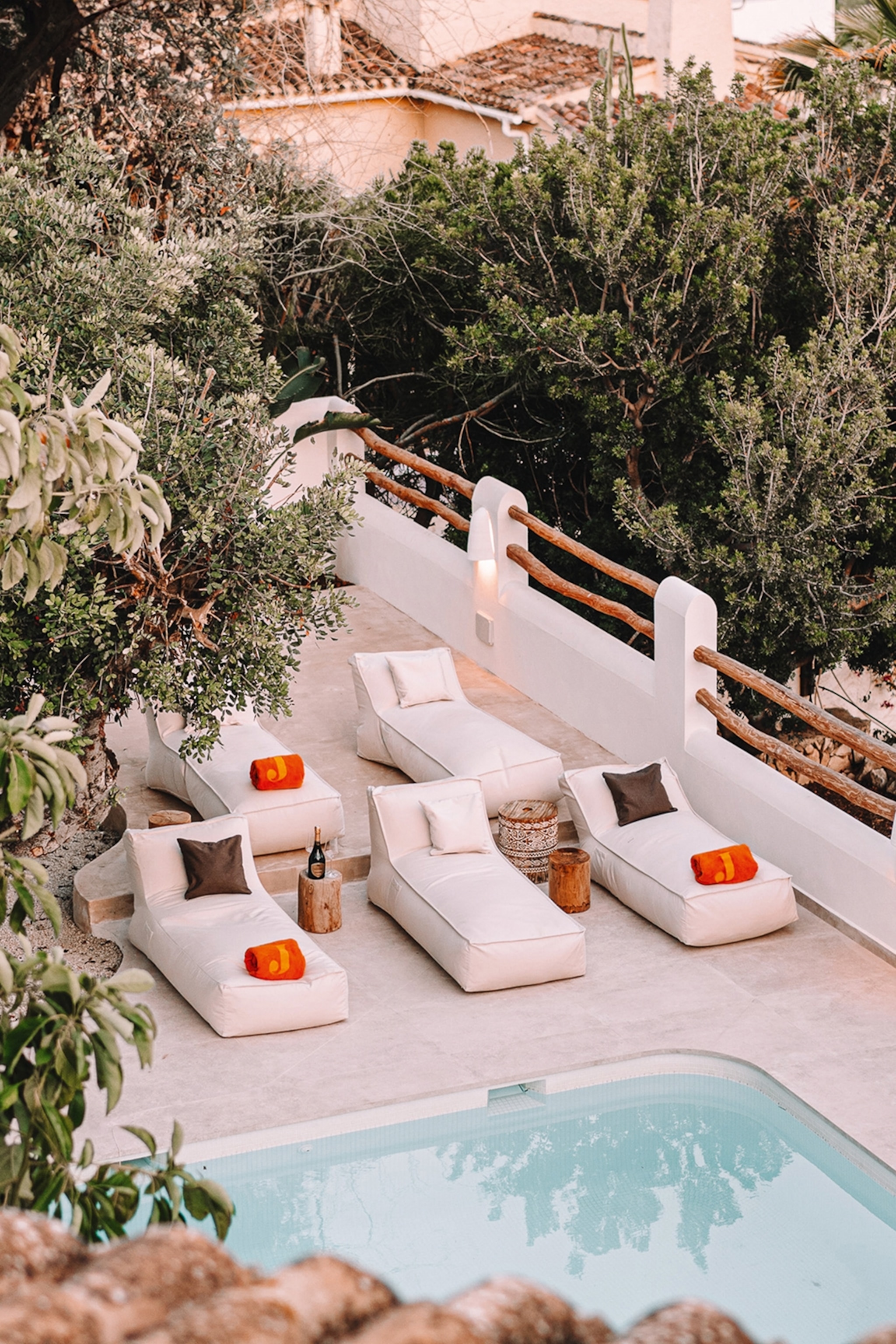 Lounging chairs on the edge of a pool shot through tropical plants.