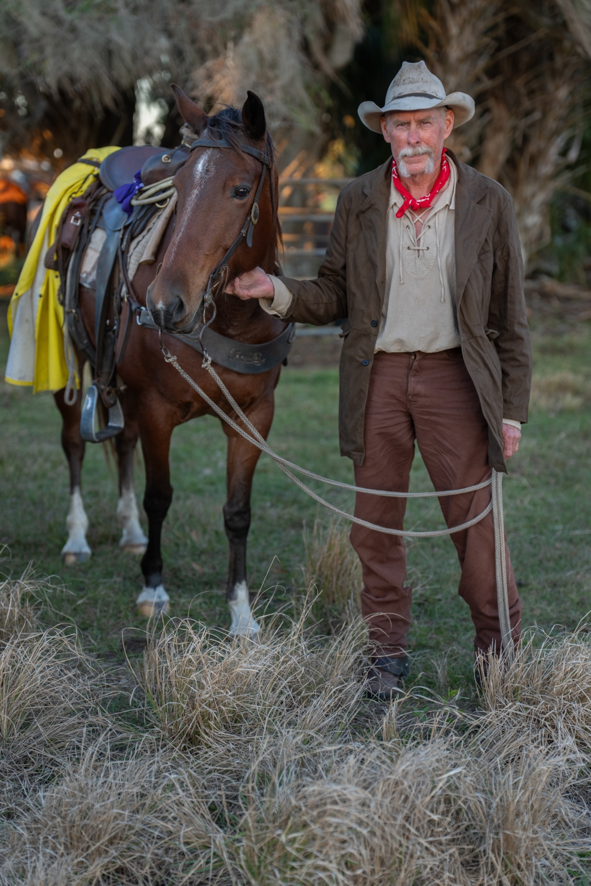 A man holds the reigns of his horse while standing next to it for a photograph.