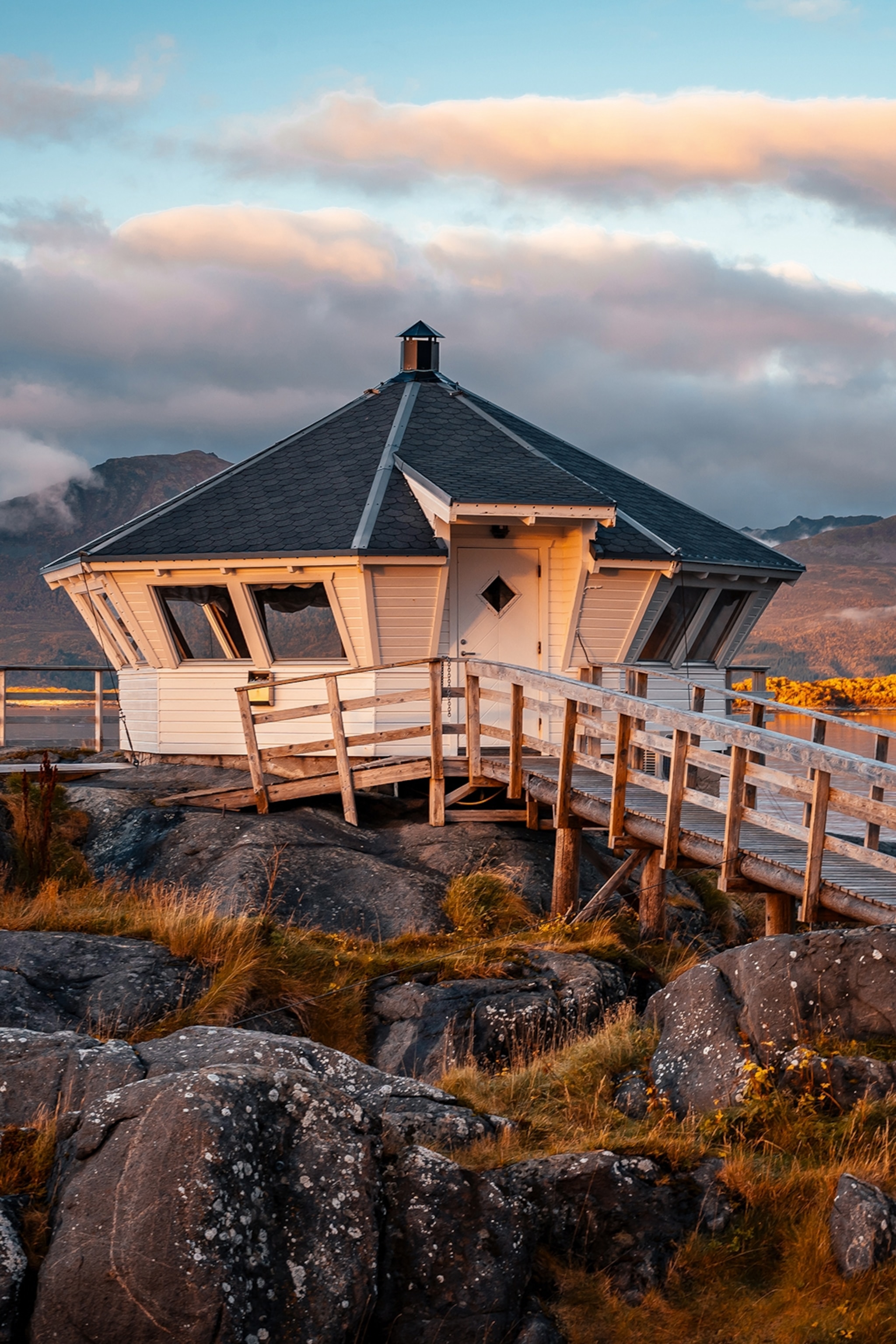 An octagonal hut built on top of a rocky landscape with a wooden walkway leading to it.