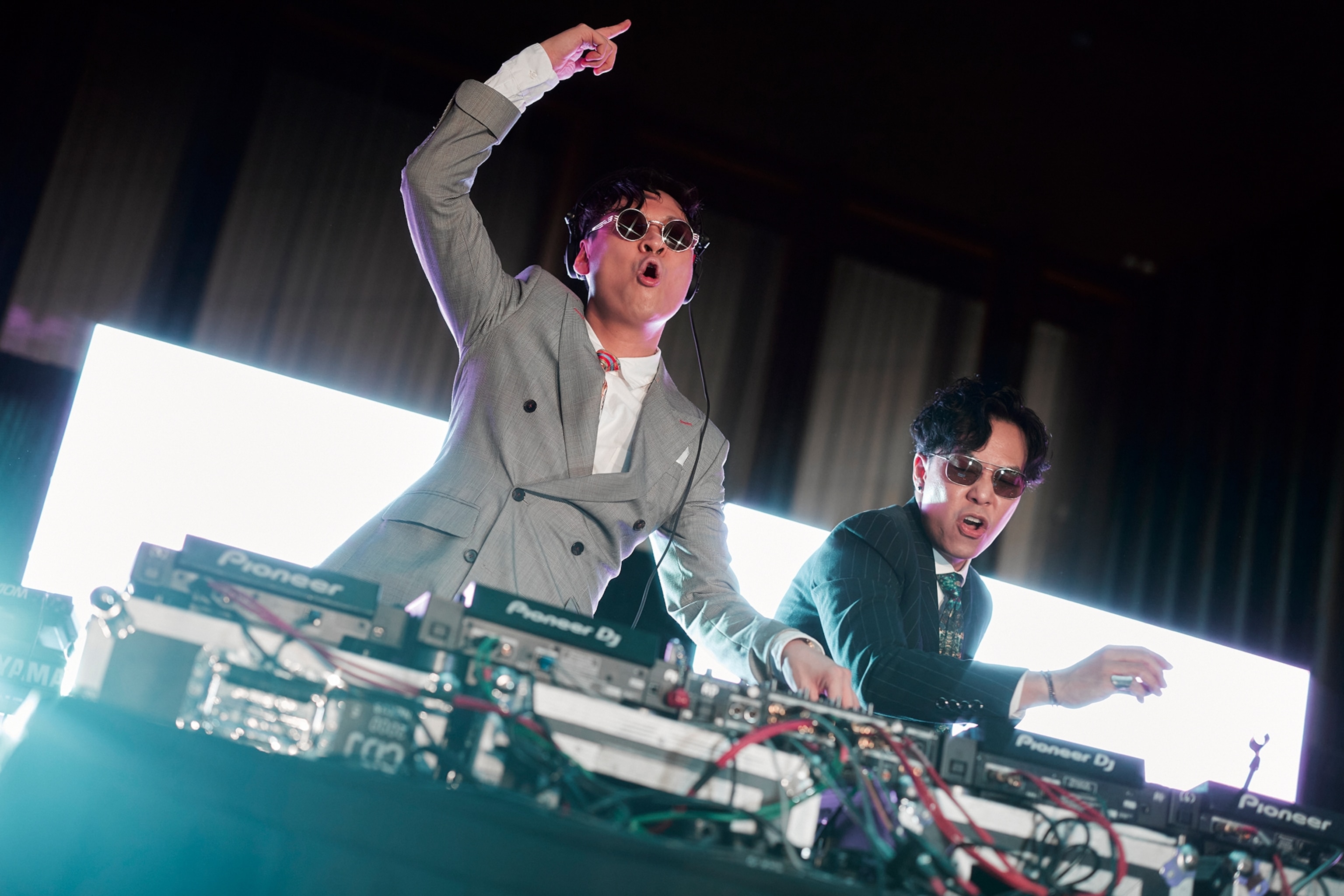 Two men in suits working a DJ deck at a party.