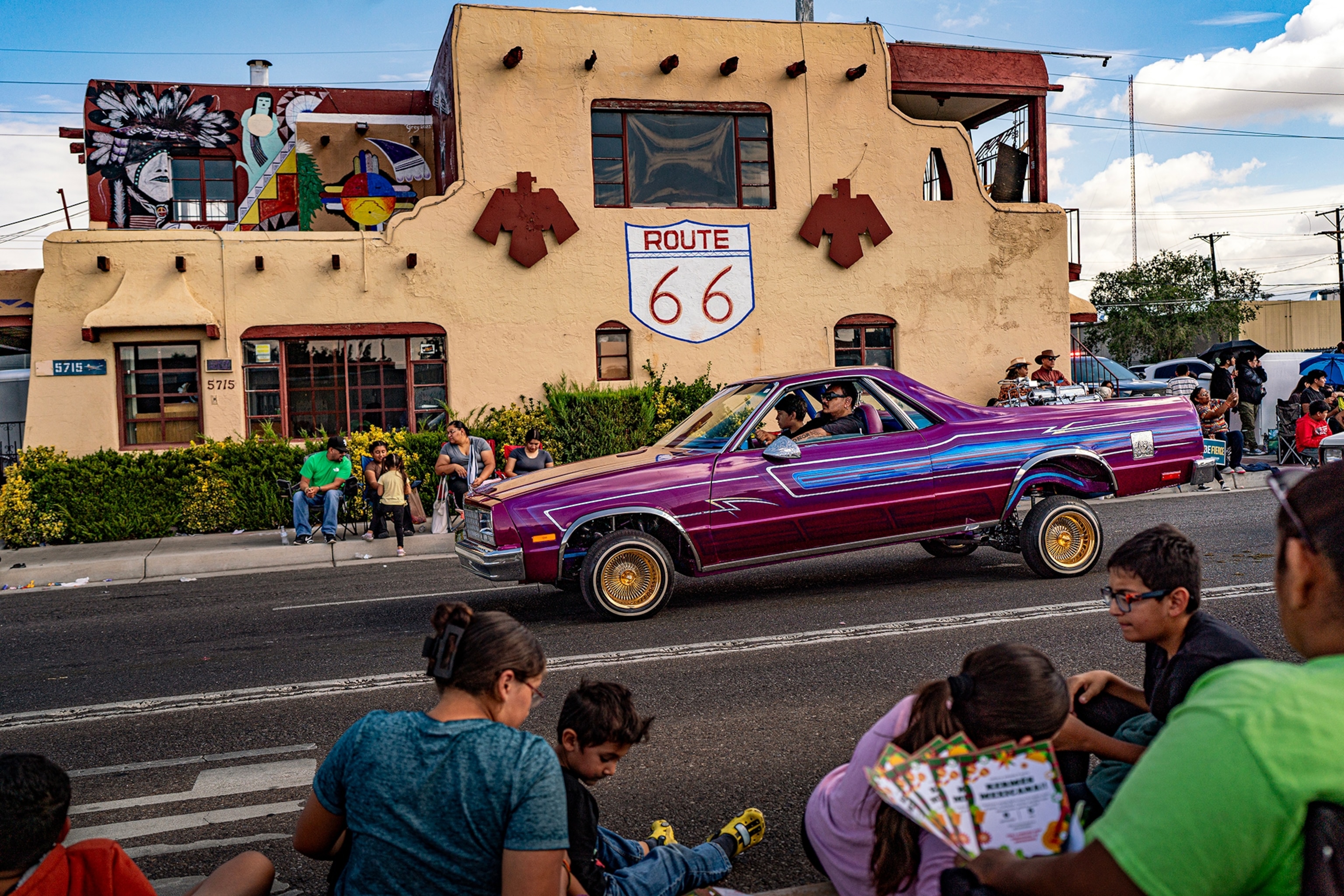 A flashy car with bouncy back wheels driving down an avenue past spectators at a parade.