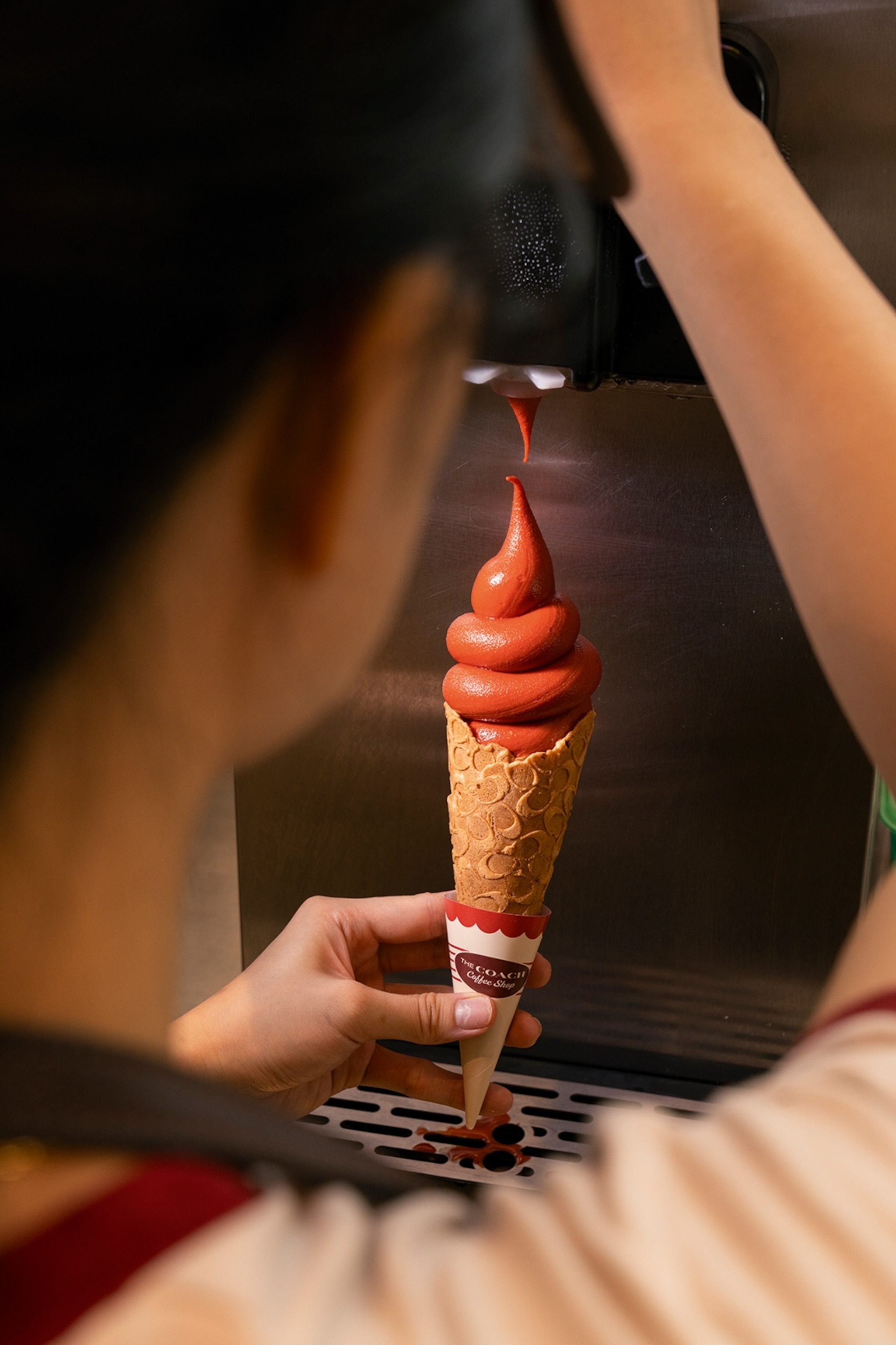 An over-the-shoulder shot of a woman pouring a soft-serve ice cream in a cone.