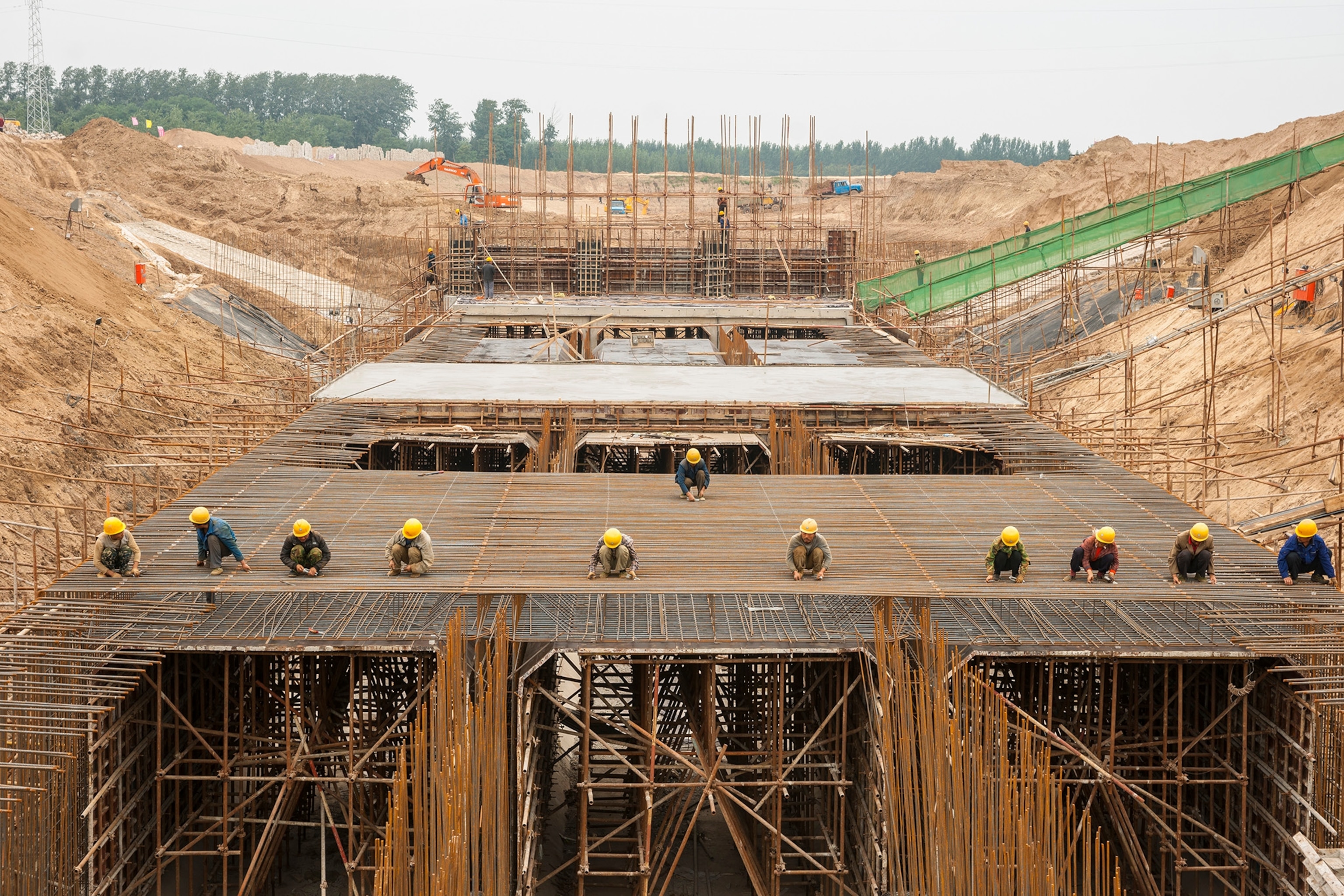 Multiple people wearing hardhats stand atop a outdoor structure made of several pipes.
