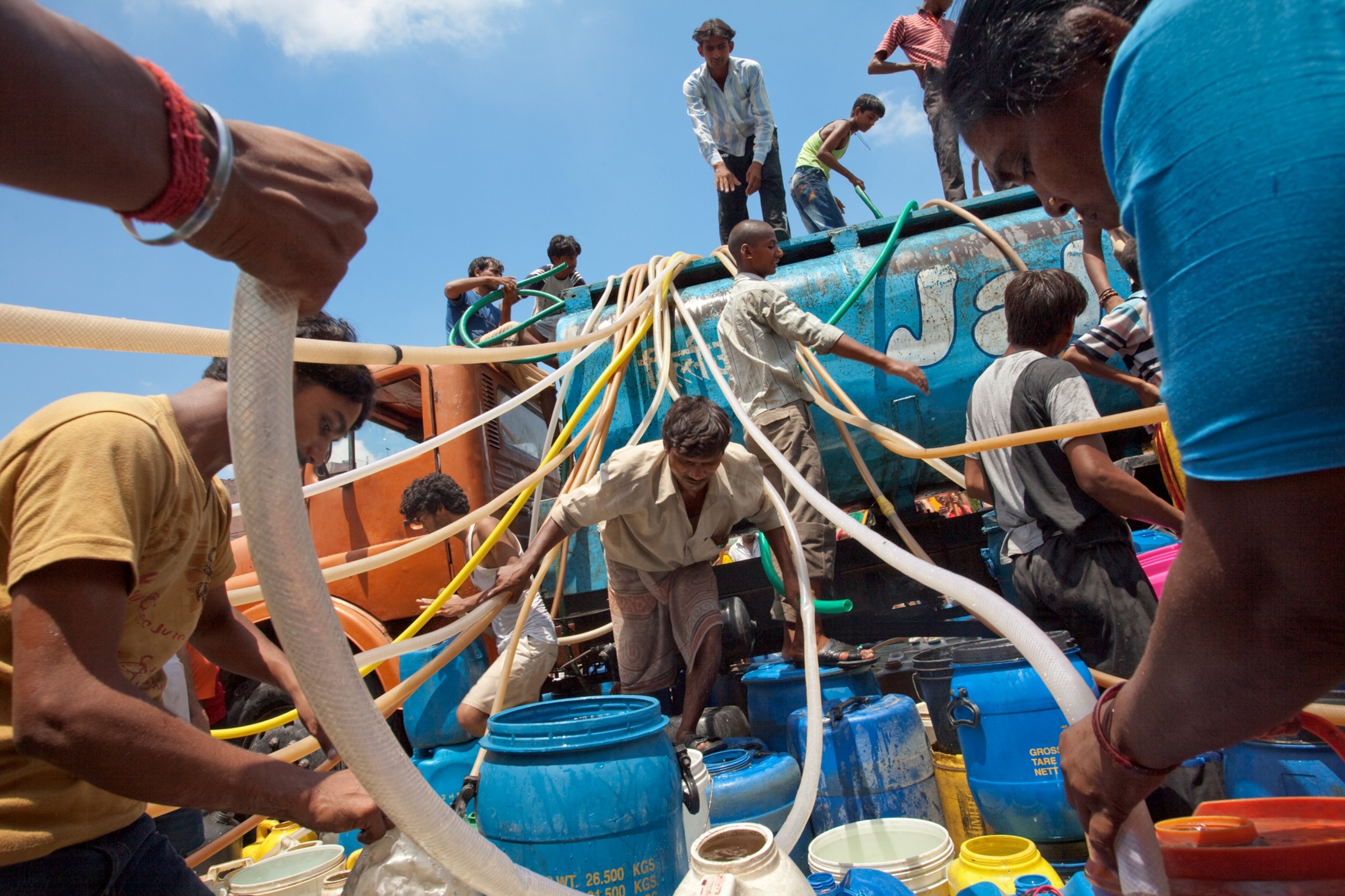 men swarming a tanker to siphon water in a Delhi slum