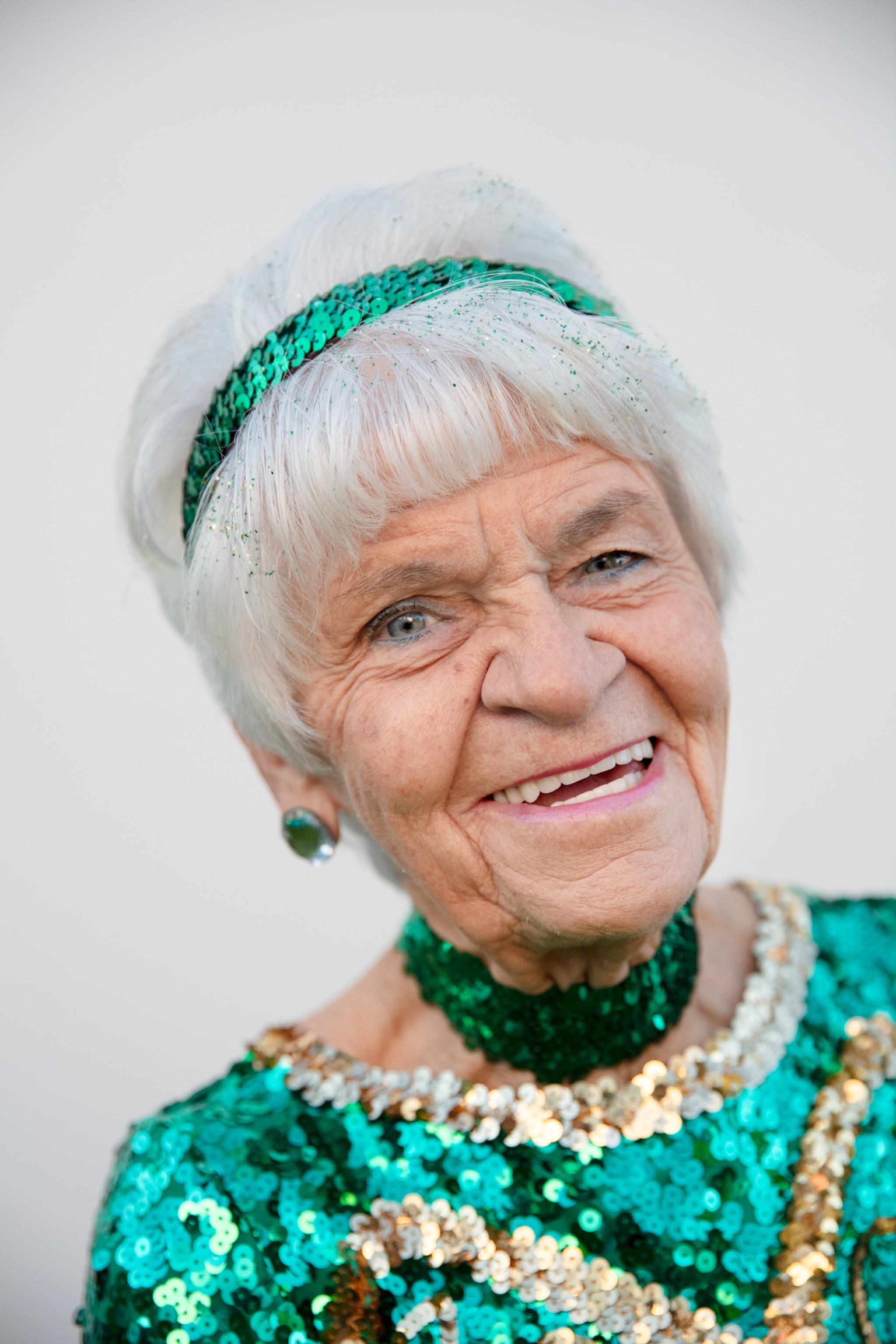 Picture of smiling woman with green hair band on grey hair.