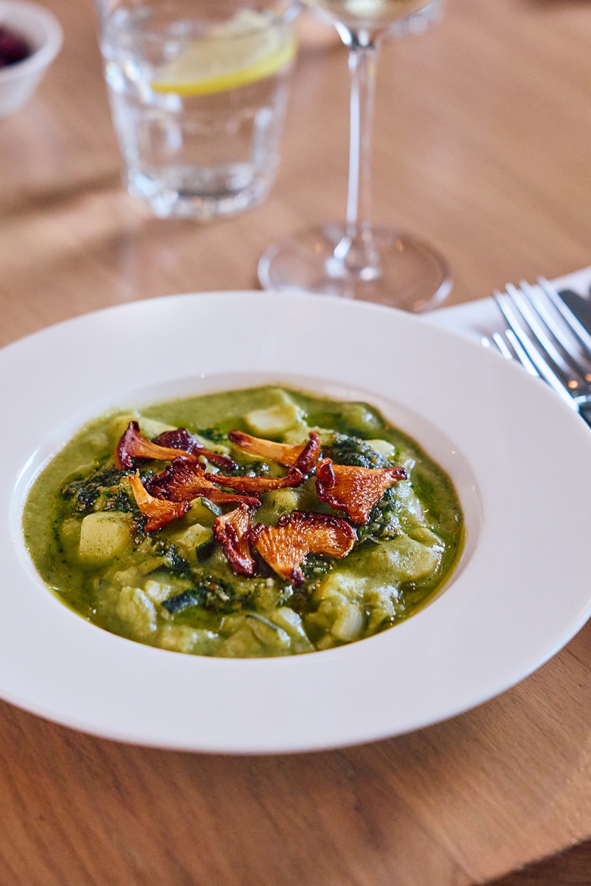 A close-up on a plate of green soup with fried oyster mushrooms on top.