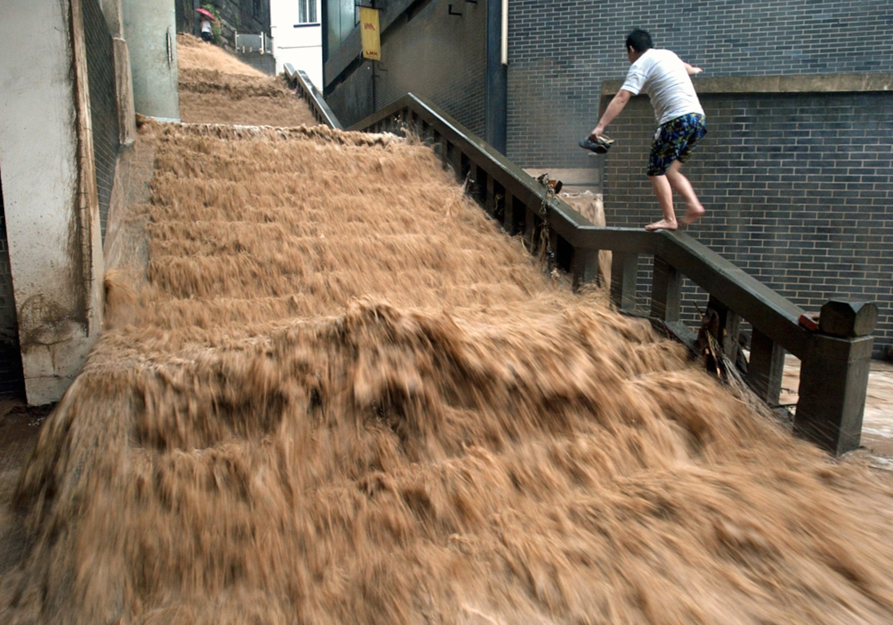 a man walking a handrail to avoid muddy floodwater in China