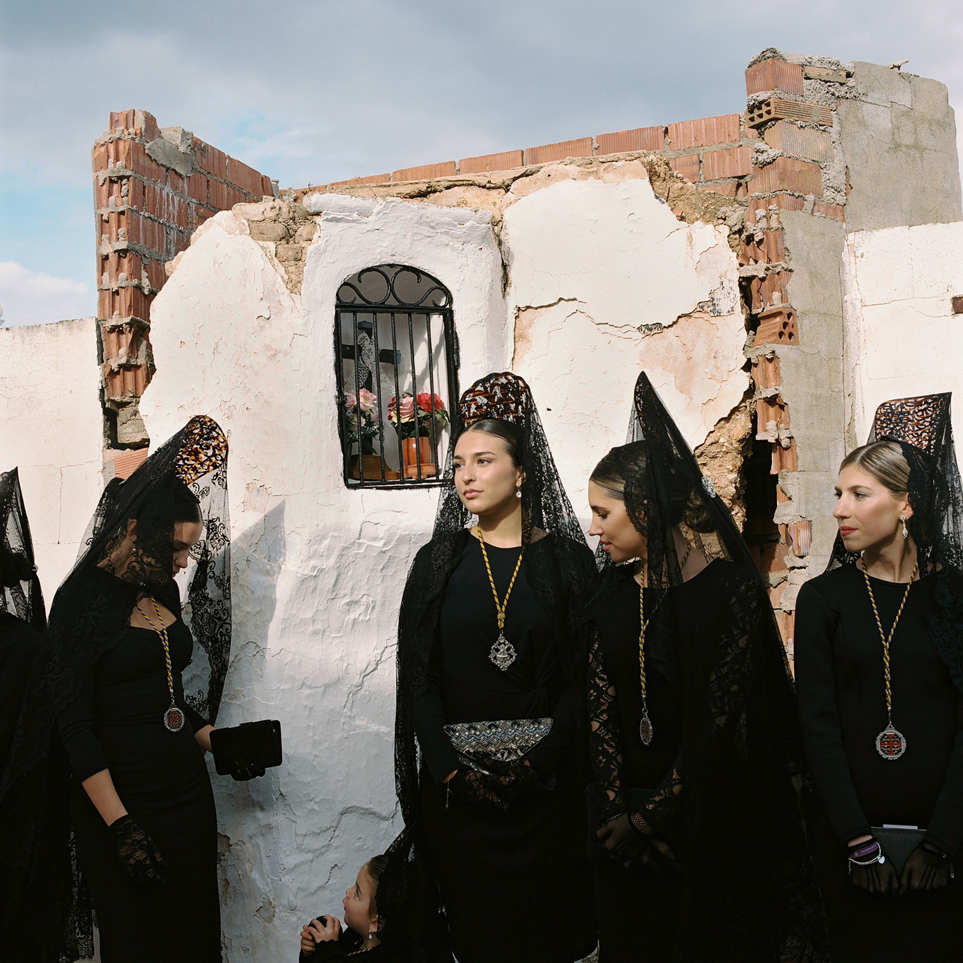 A group of women wearing lace veils in front of a building in ruins.
