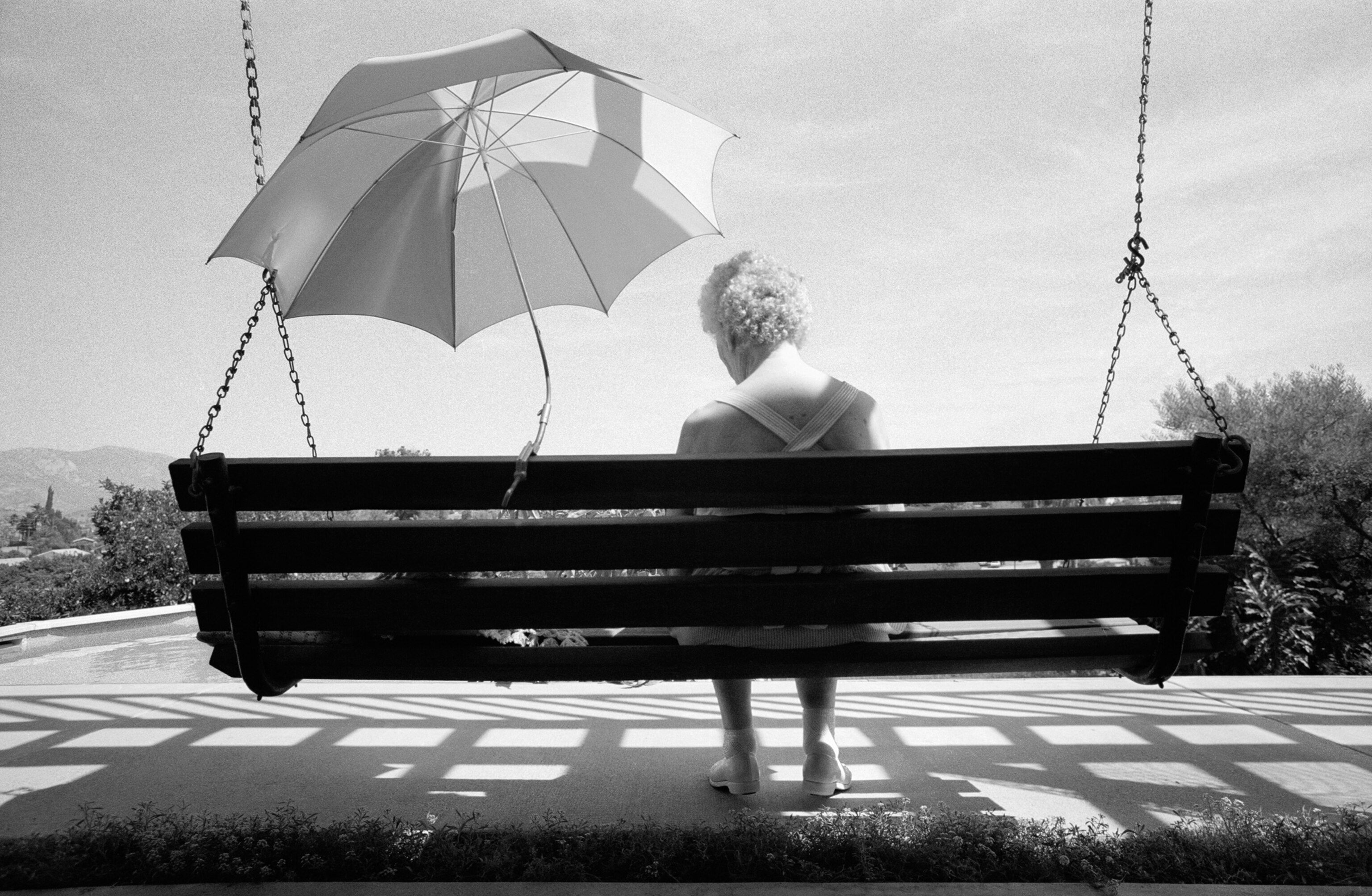 a woman with Alzheimer's siting on a swing shaded by an umbrella.