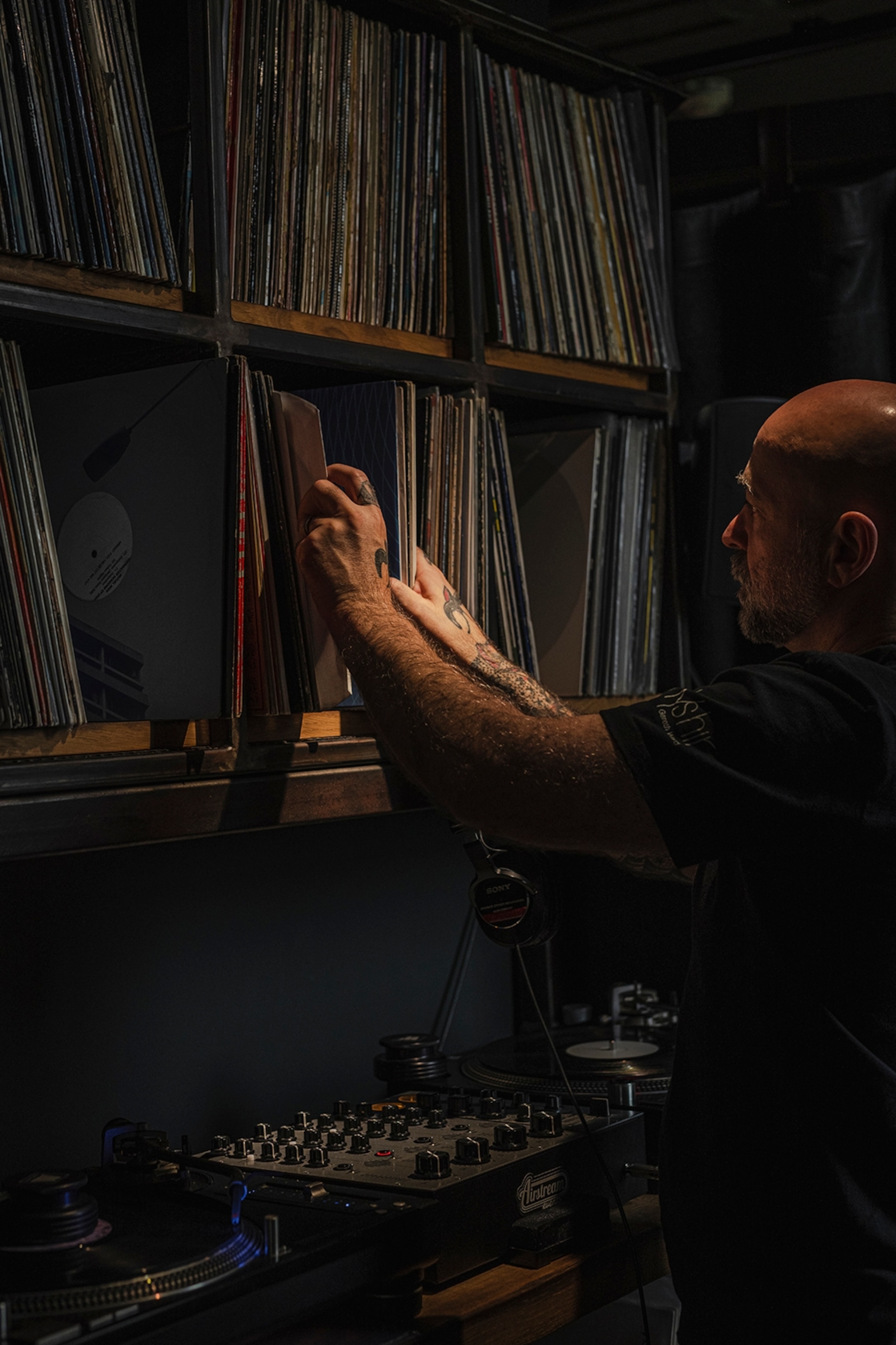 A bald, middle-aged man picking out vinyl from a low-lit shelving unit.