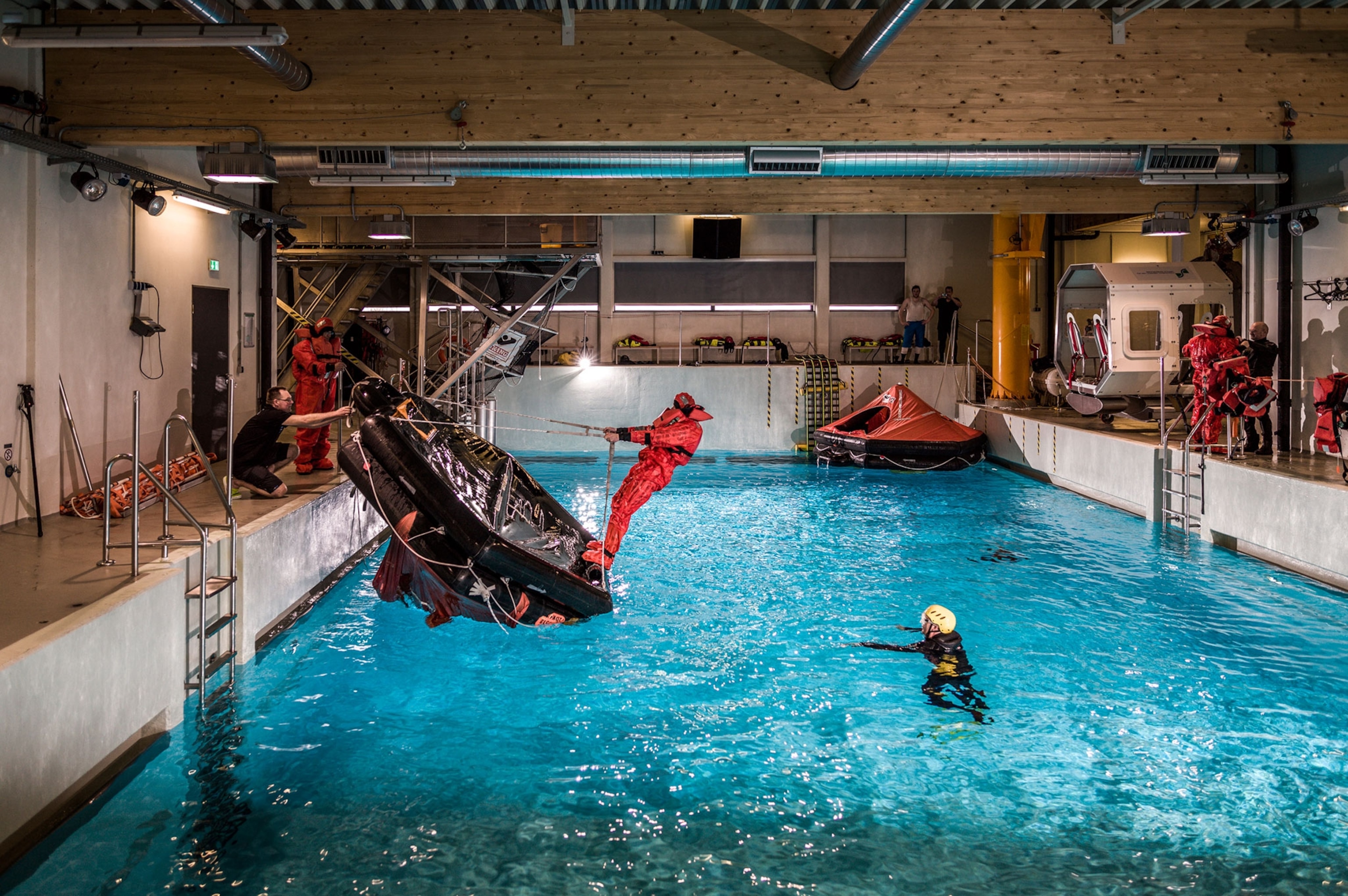 a trainee preparing to flip a life raft into a pool as his instructors look on