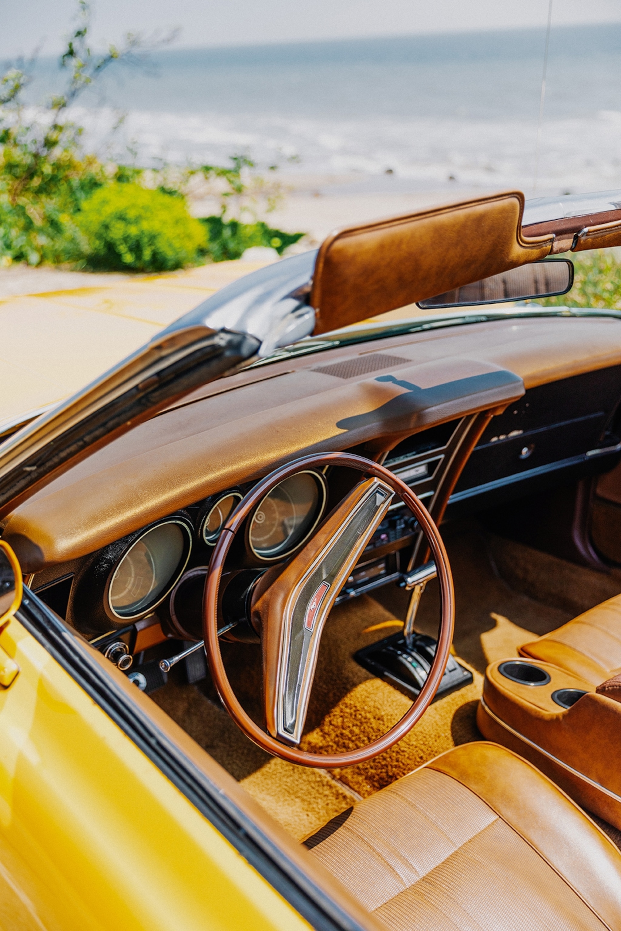 The interiors of a chic, retro car with a velvet cushioning, mahogany wood decor and a sleek steering wheel.