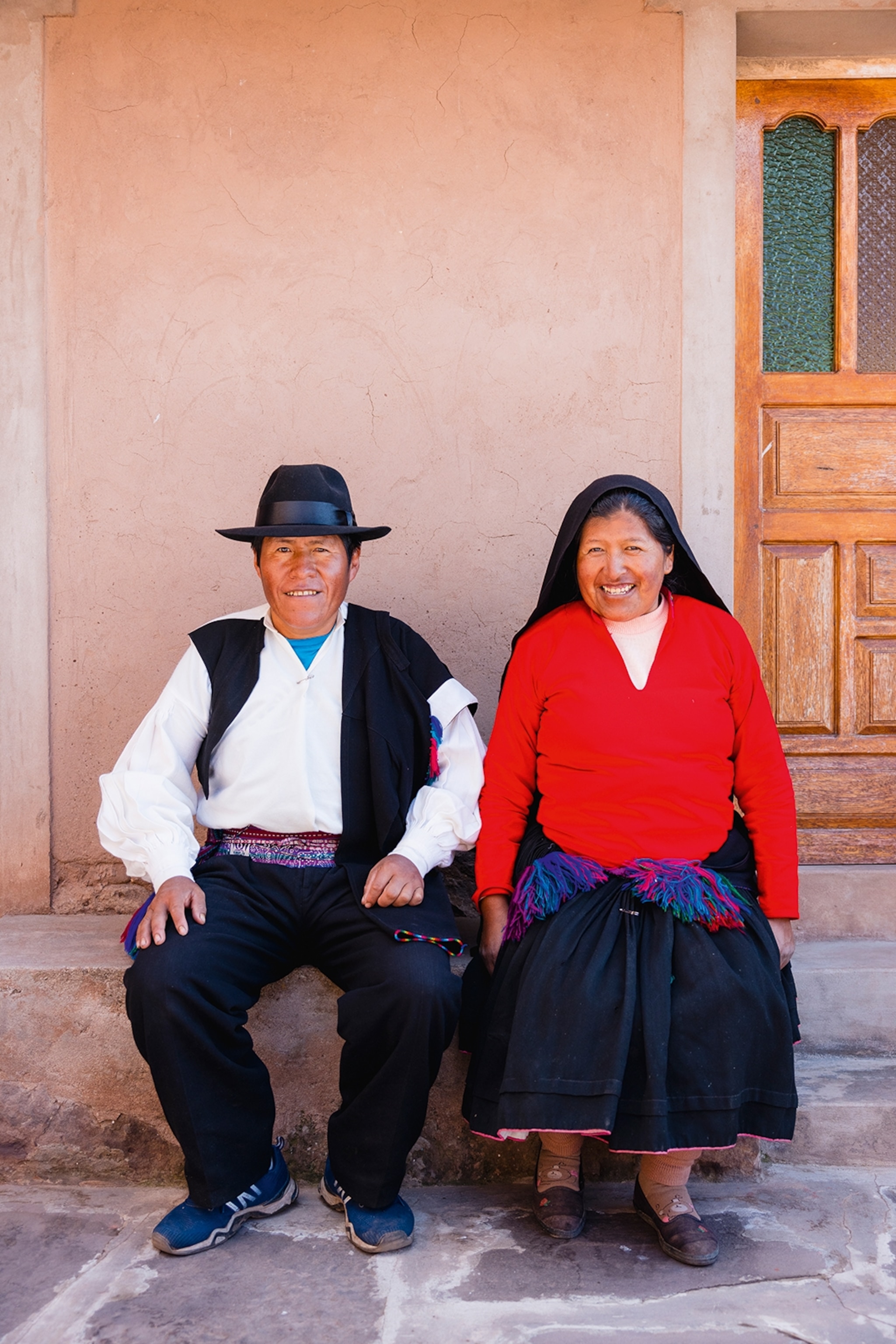 A friendly Peruvian couple sat on a bench outside their home and posing for a portrait.
