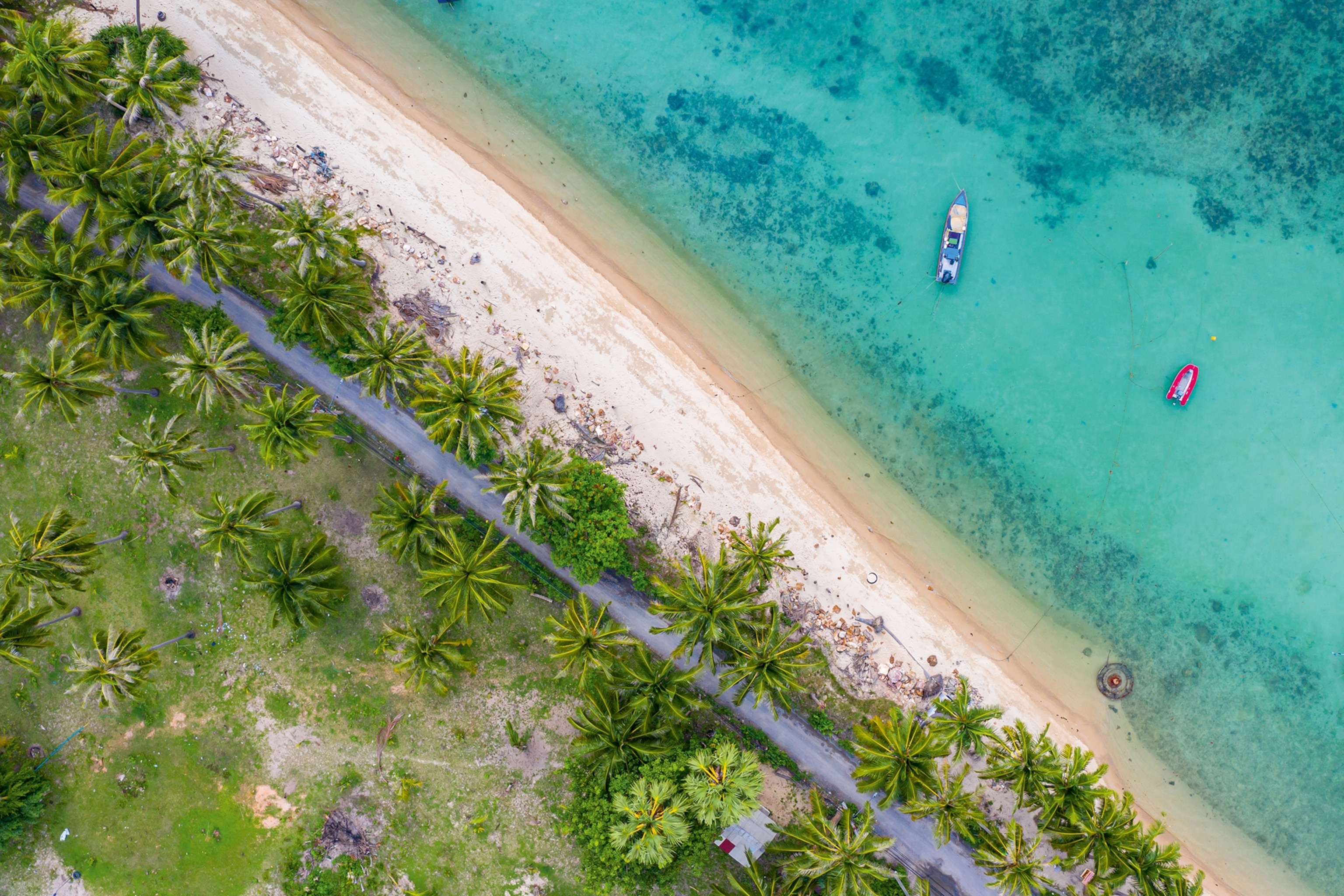 A sandy beach with a boat anchored off-shore in the ocean, shot from above.
