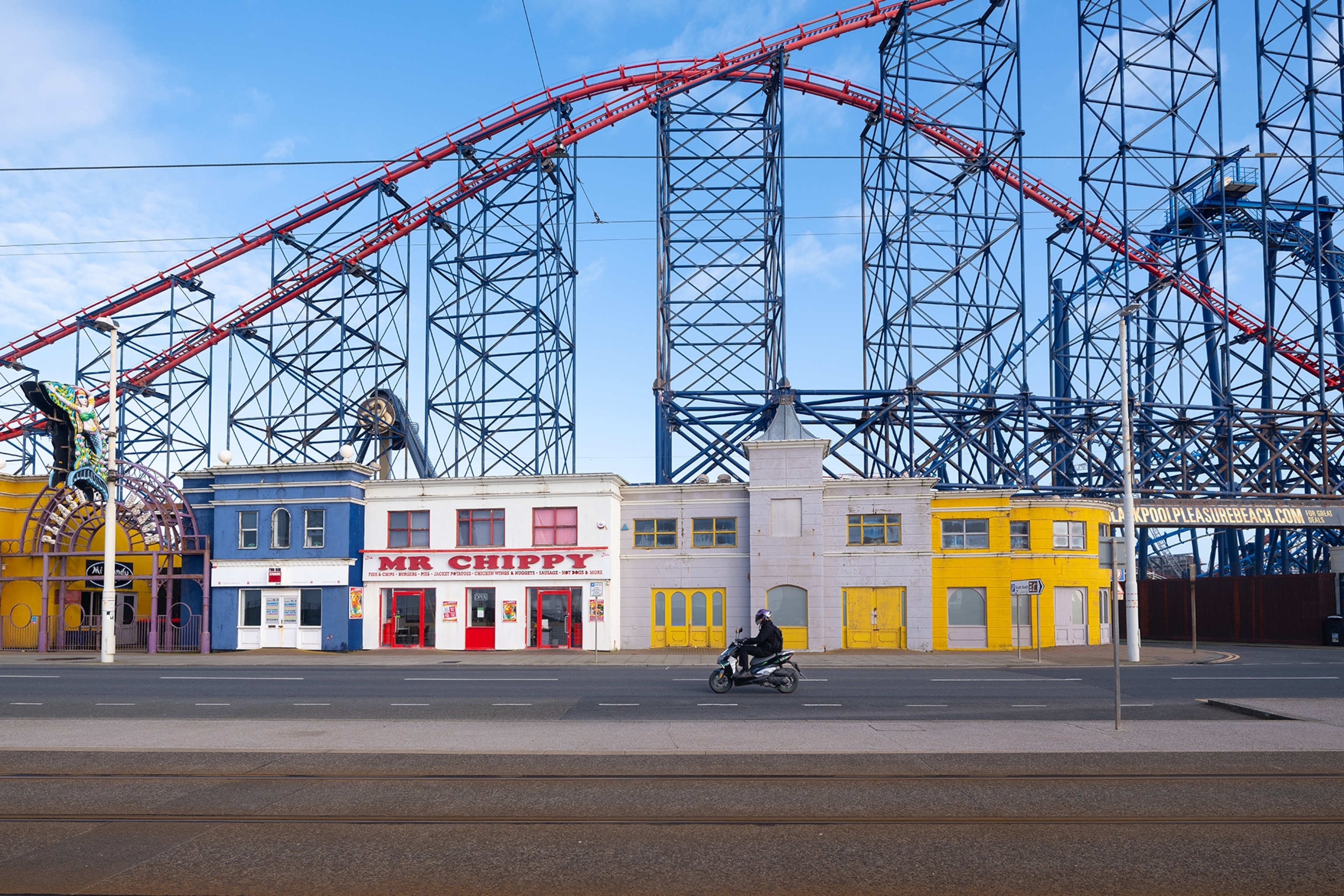 A quiet street showing British fish and chips shops with an empty rollercoaster in the background.