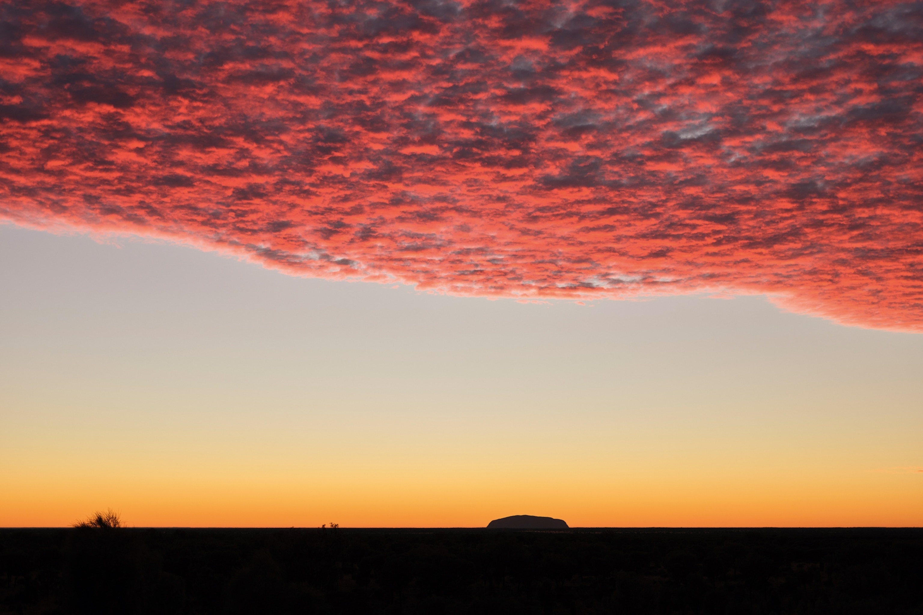 A single rock formation in the Australian Outback at sunset.