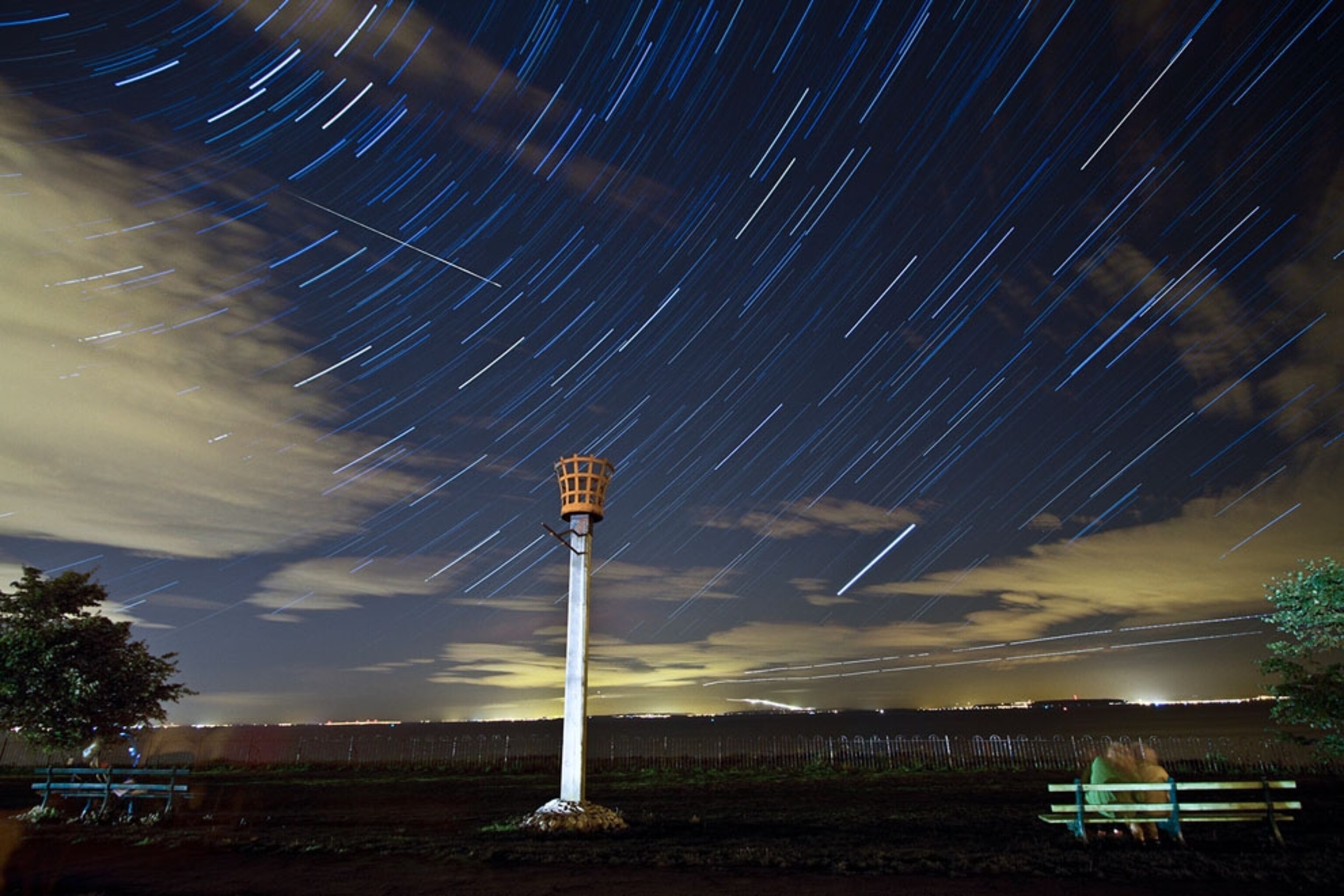 Couple sits on a bench in South Wales at night under stars