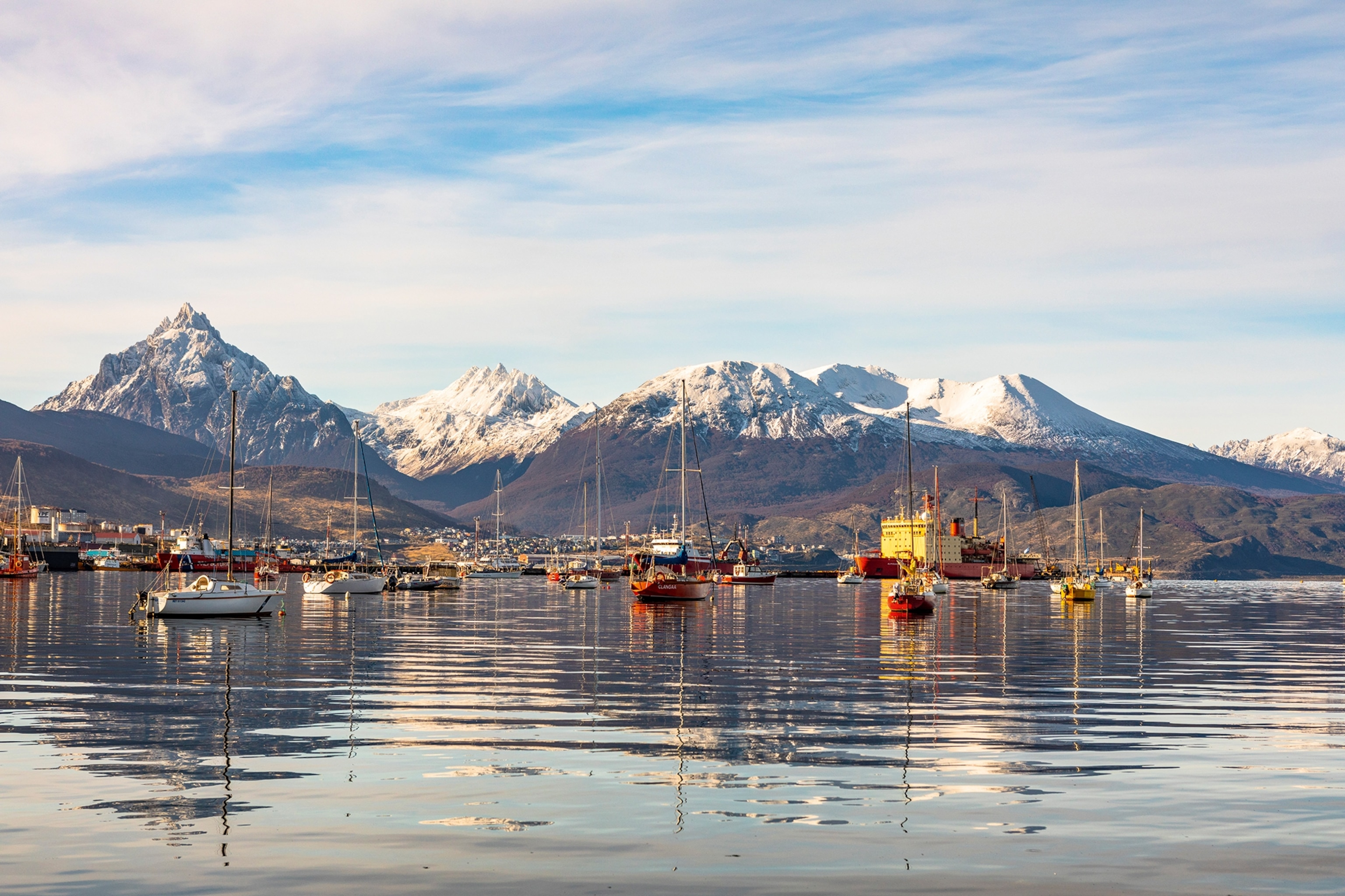 Sailboats on a body of water with snow-capped mountains in the background.