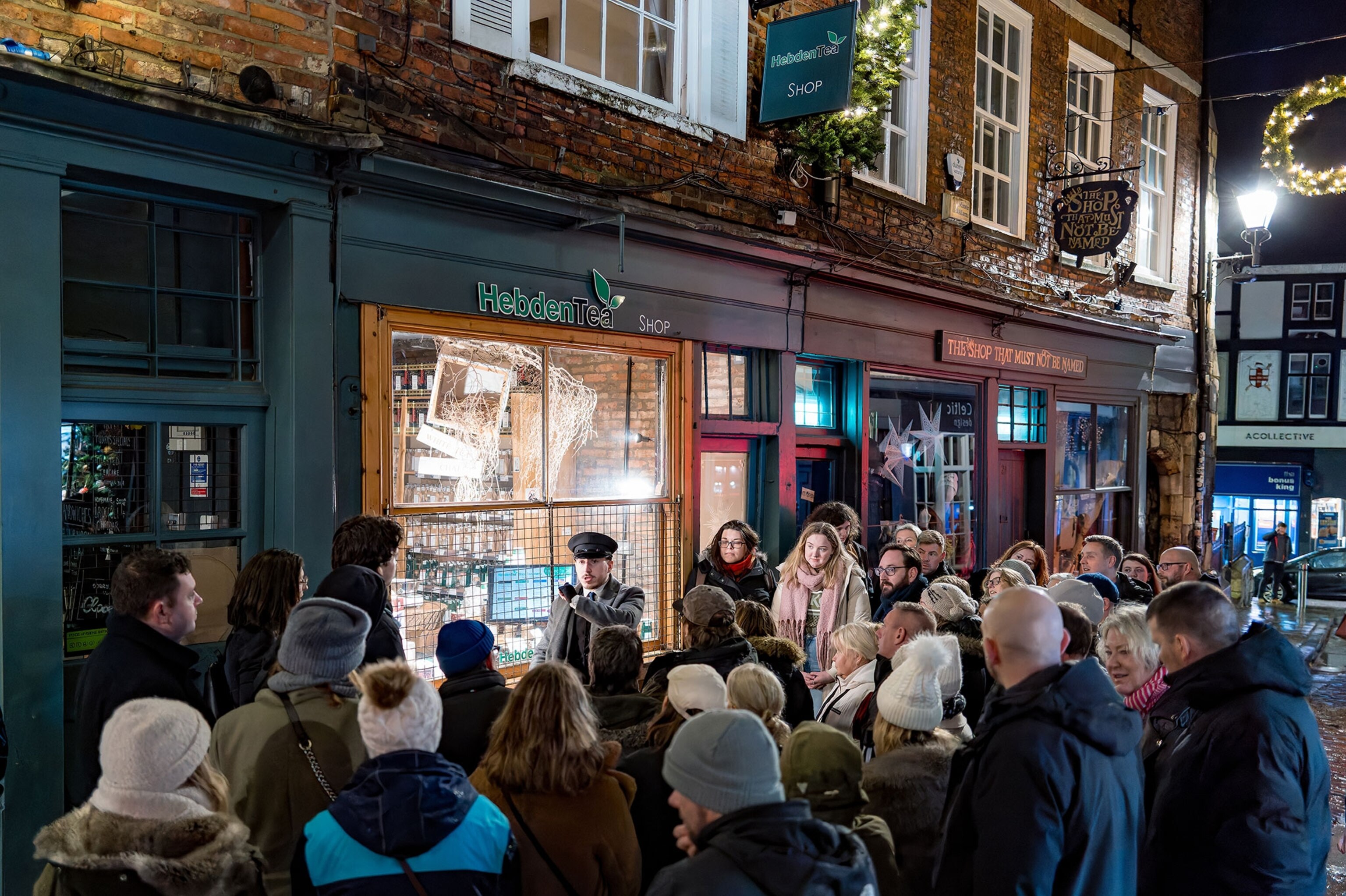 A man in a hat stands in front a a crowed of people surrounding him in front of a storefront.