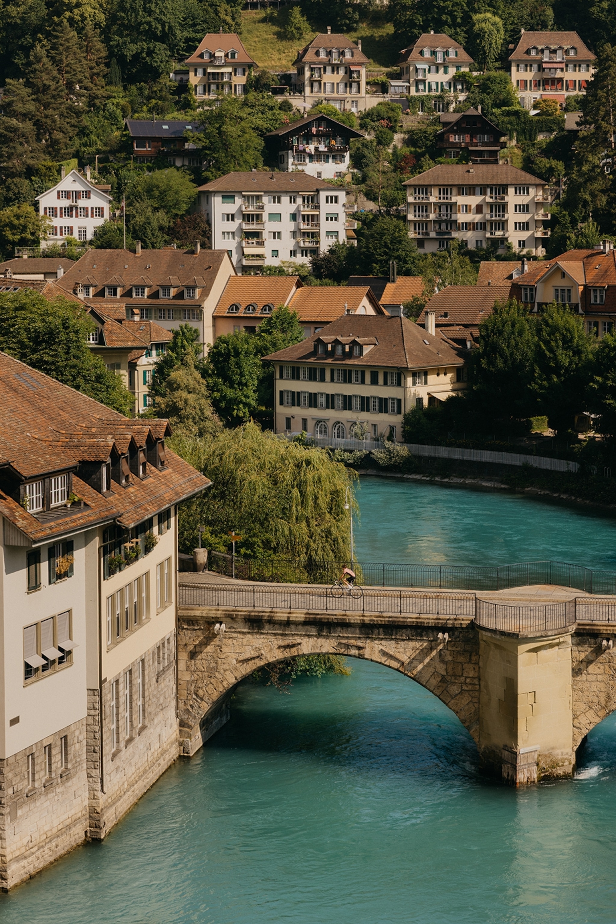 A picturesque mountain town built on multiple levels on a hill as an arched bridge cuts through a turquoise river.