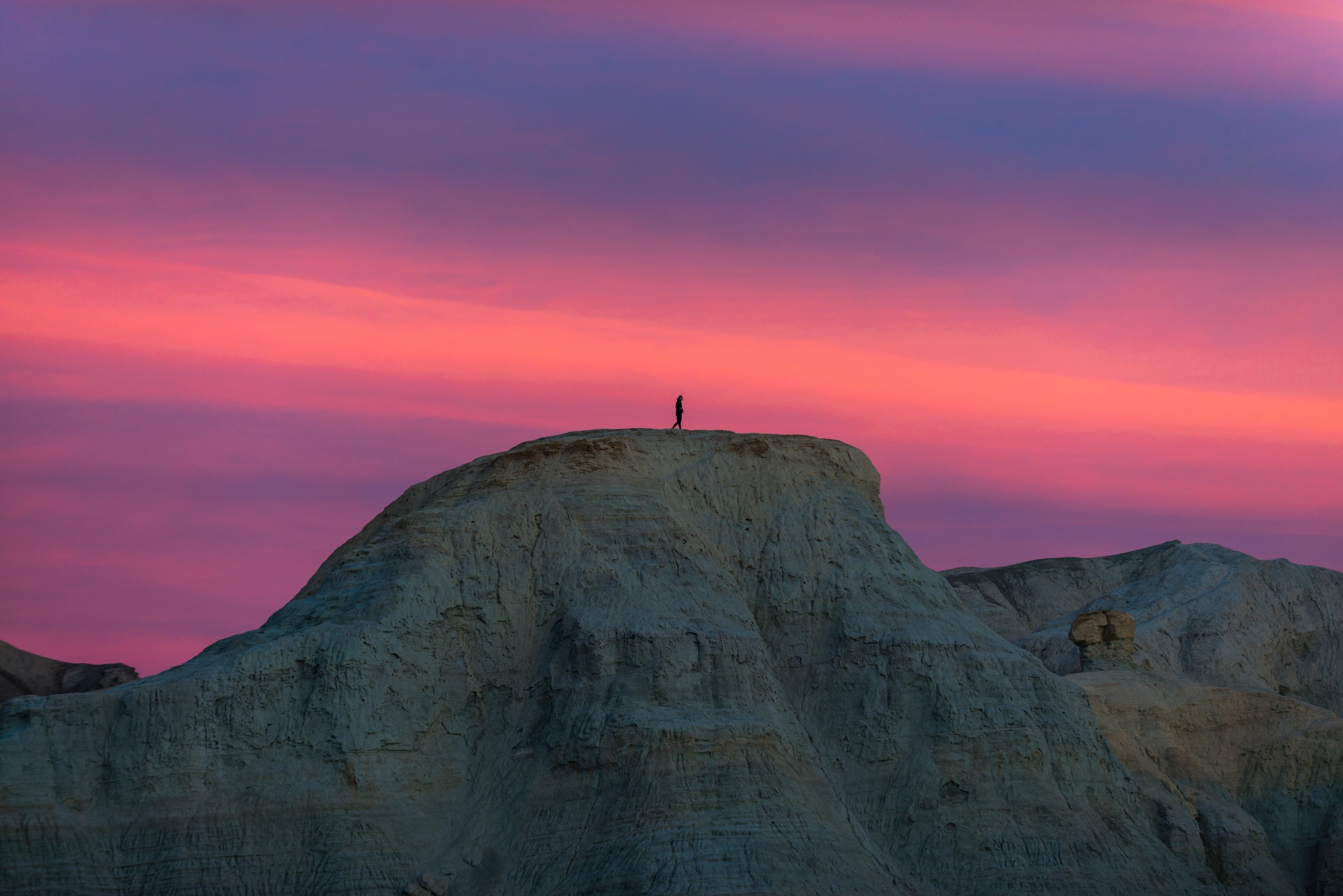 A hiker climbs a hill in Death Valley to watch a pink sunset.