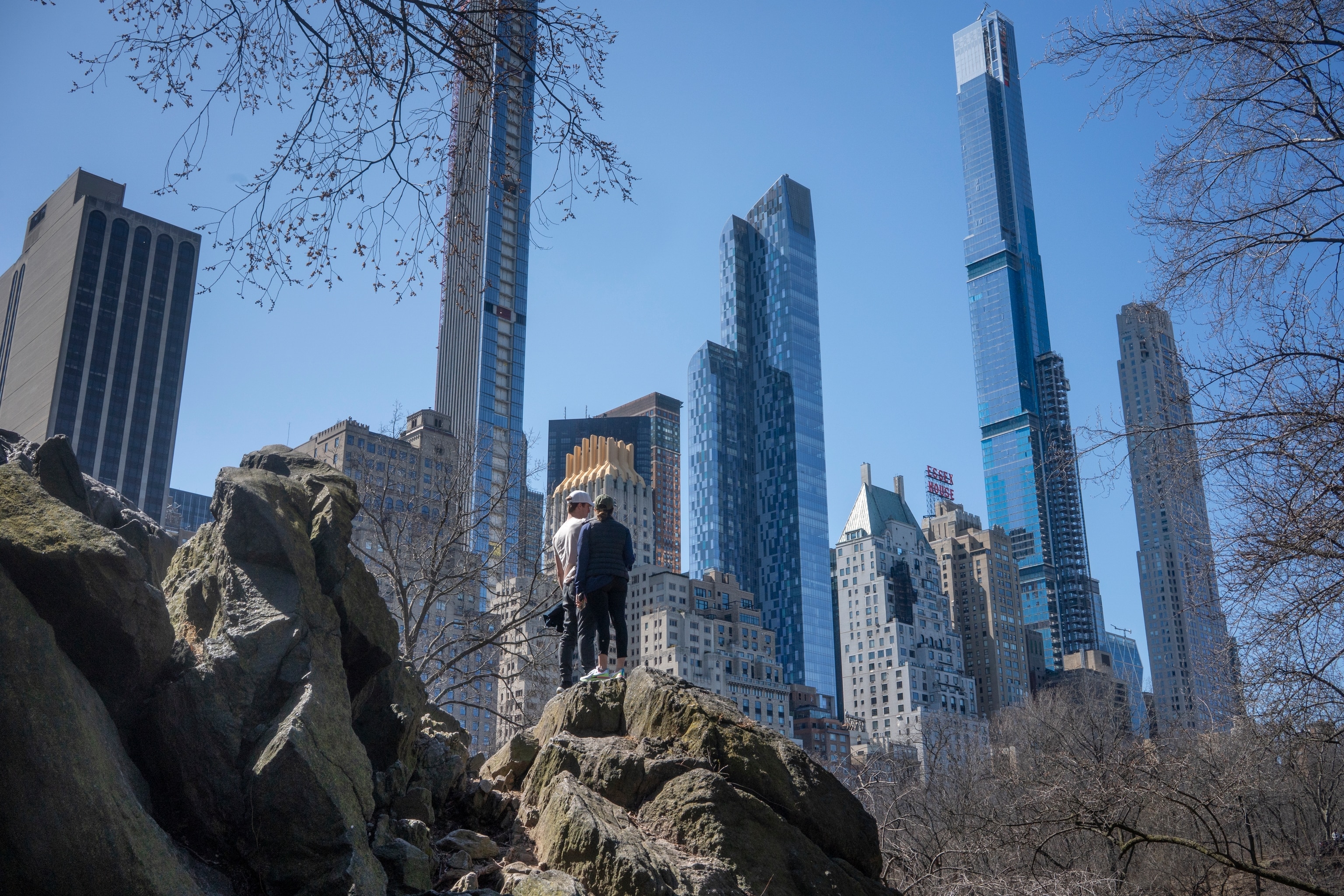 Two people stand on a large rock while looking at the cityscape of New York City