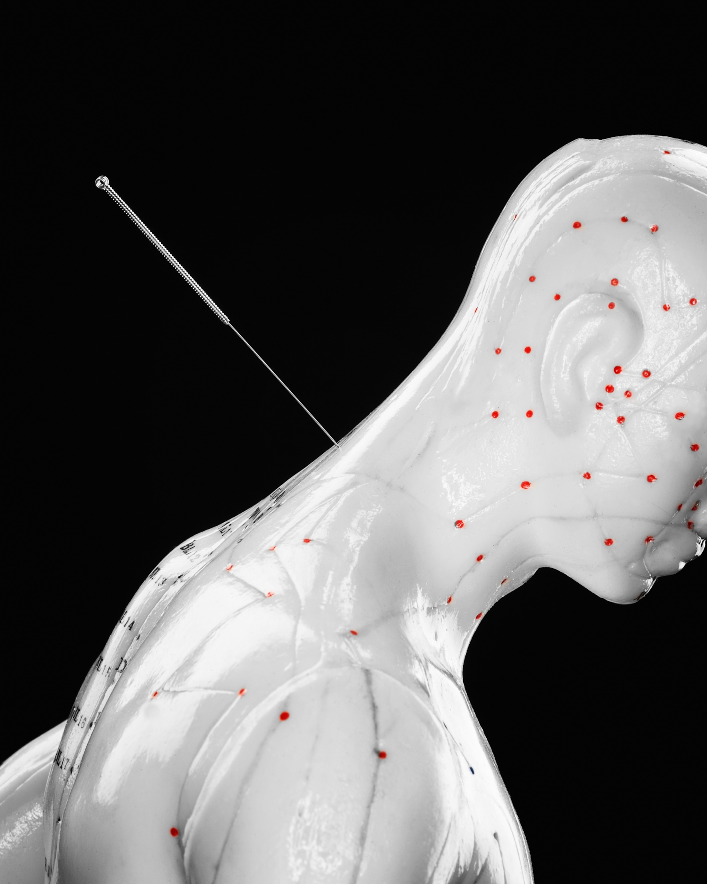 an acupuncture model with needle sticking the base of its neck, against black background