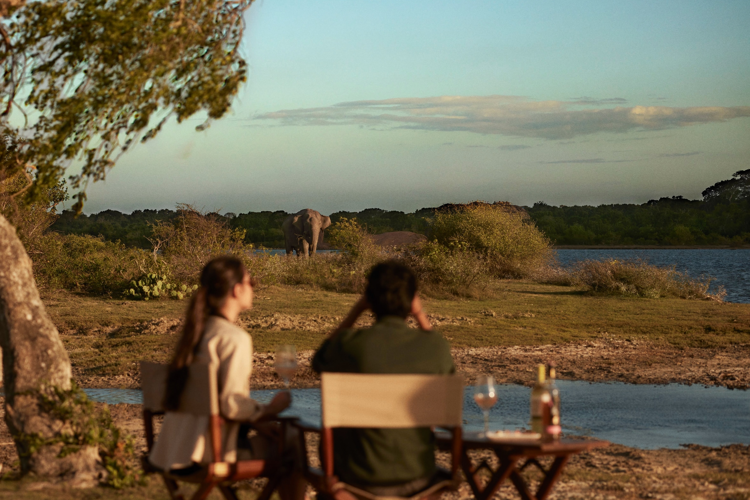 Two people sit on a bench, looking out over a lake.