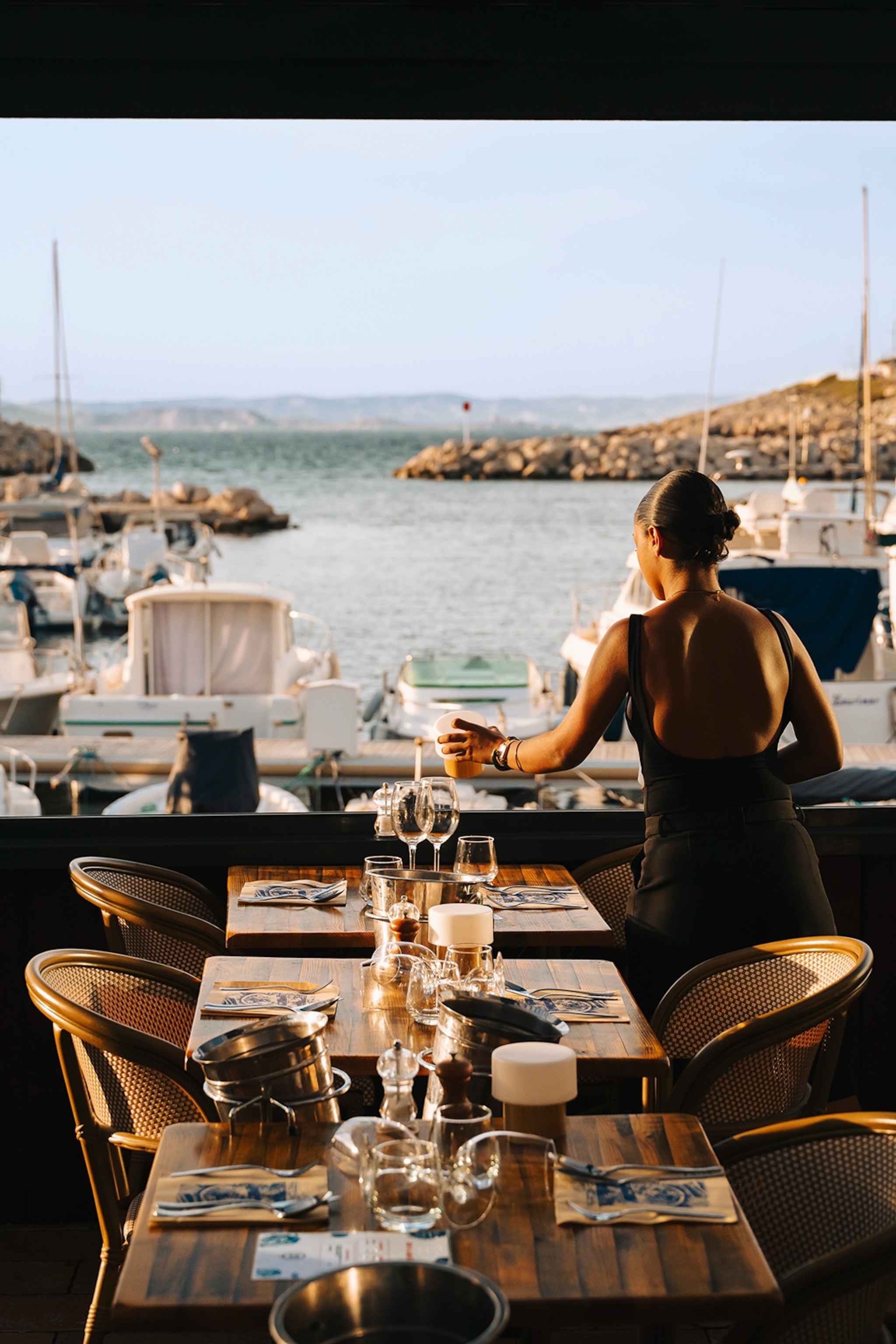 A waitress setting a line of tables with views over a harbour.