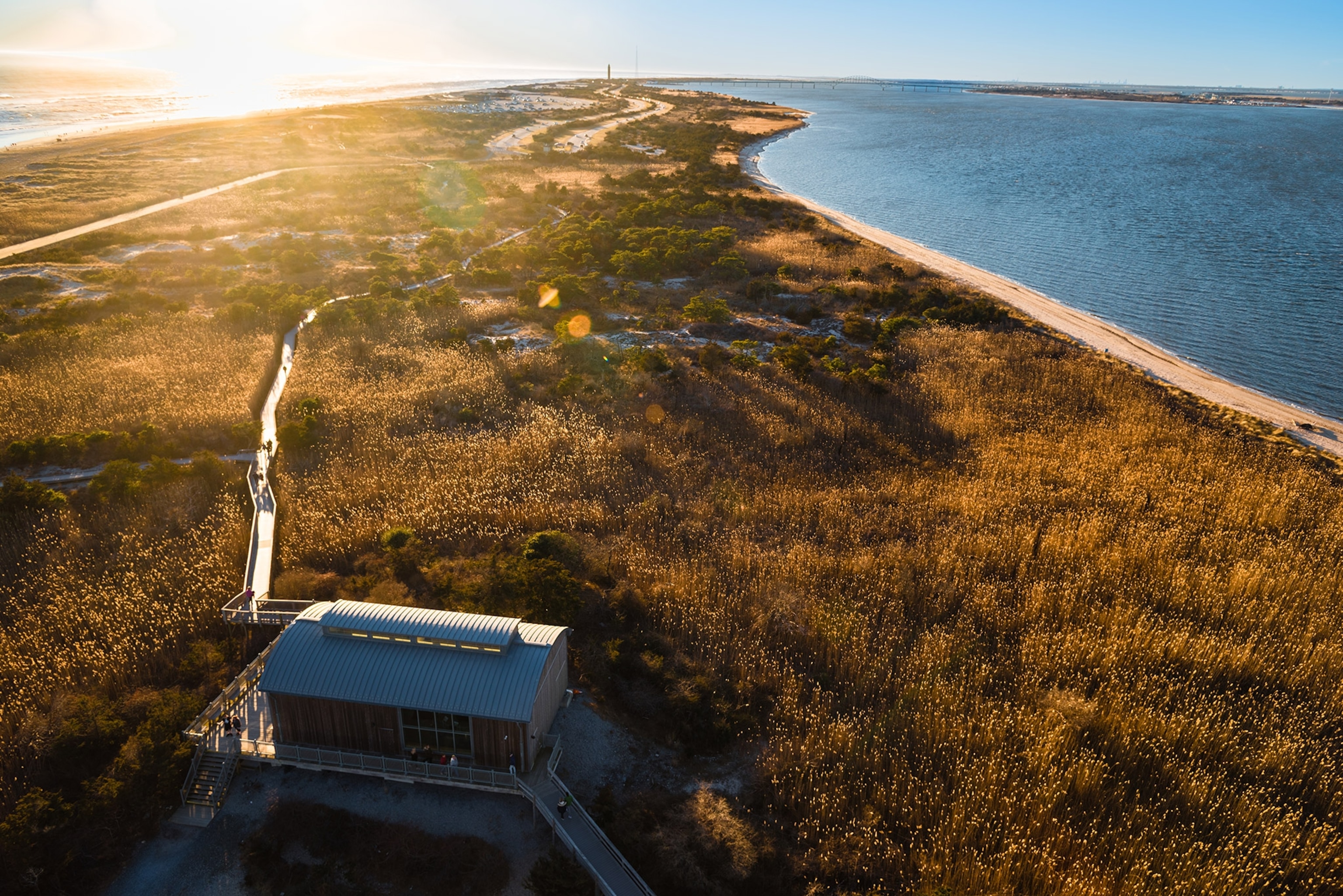 Aerial view of a natural area of reeds along the ocean with boardwalk running through, a structure in the foreground