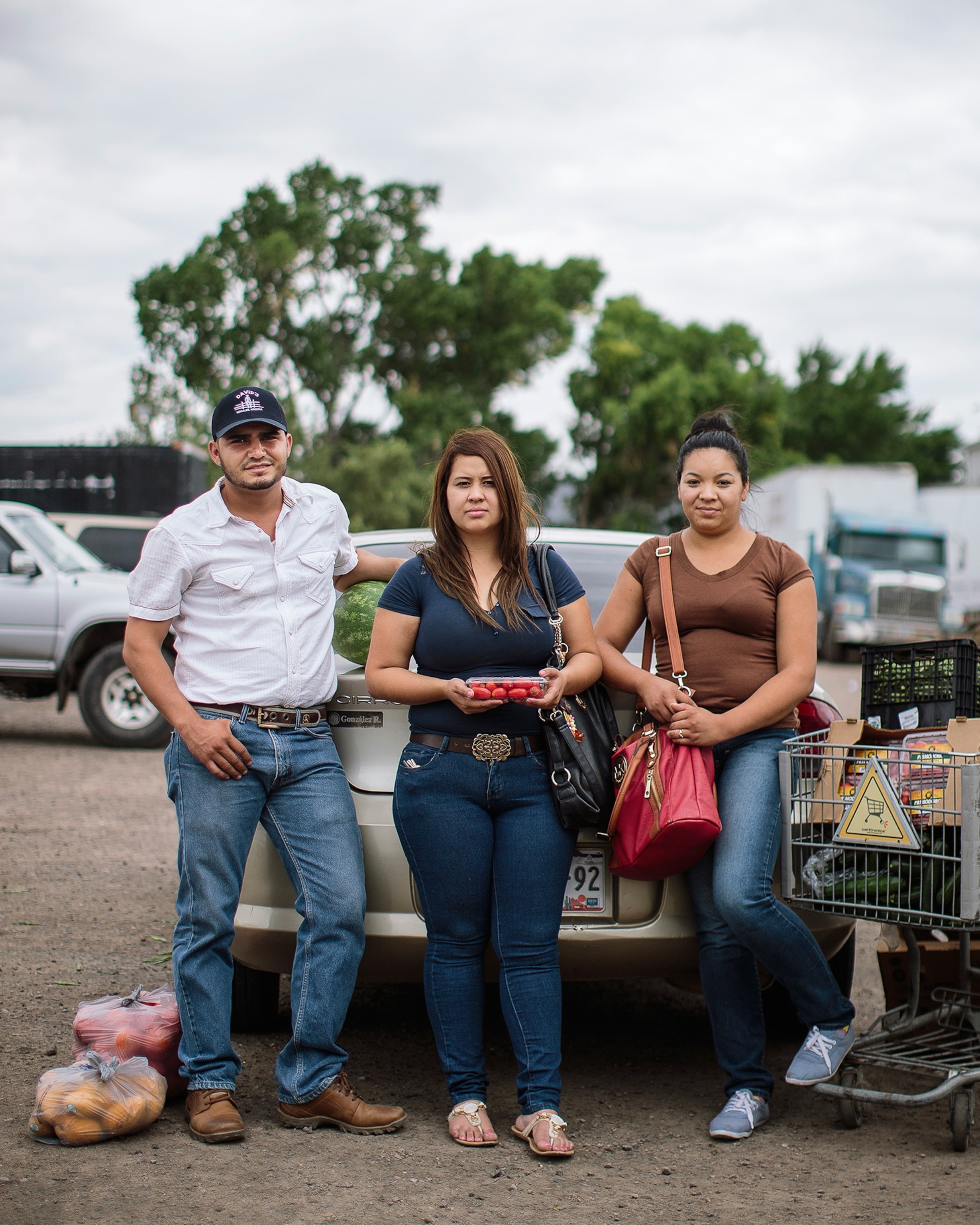 (Left to Right) Reyna Cantua, Luis Enriquez, and Ana Cristina Rey, citizens of Mexico, pick up food in the lot of Borderlands Food Bank in Nogales, Arizona. Photograph by Bryan Schutmaat