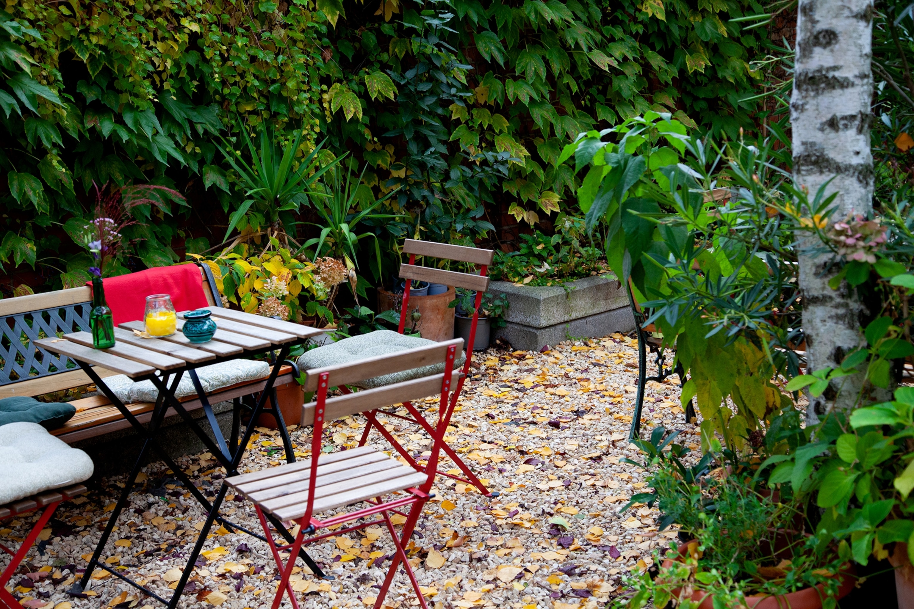 A gravelstone cafe terrace with simple, foldable chairs and a hedge.