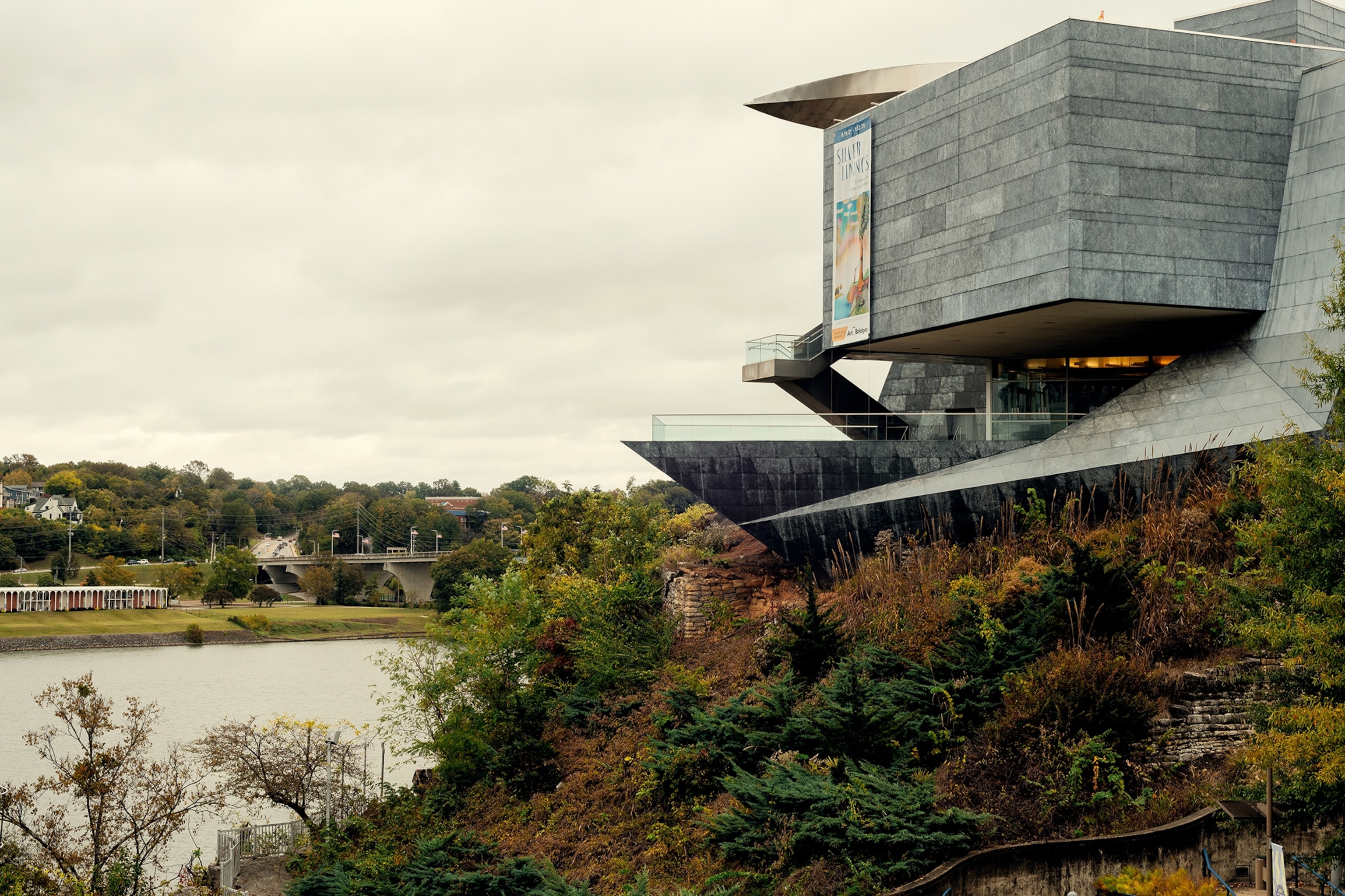 A modernist art museum on a small overhang by a river.