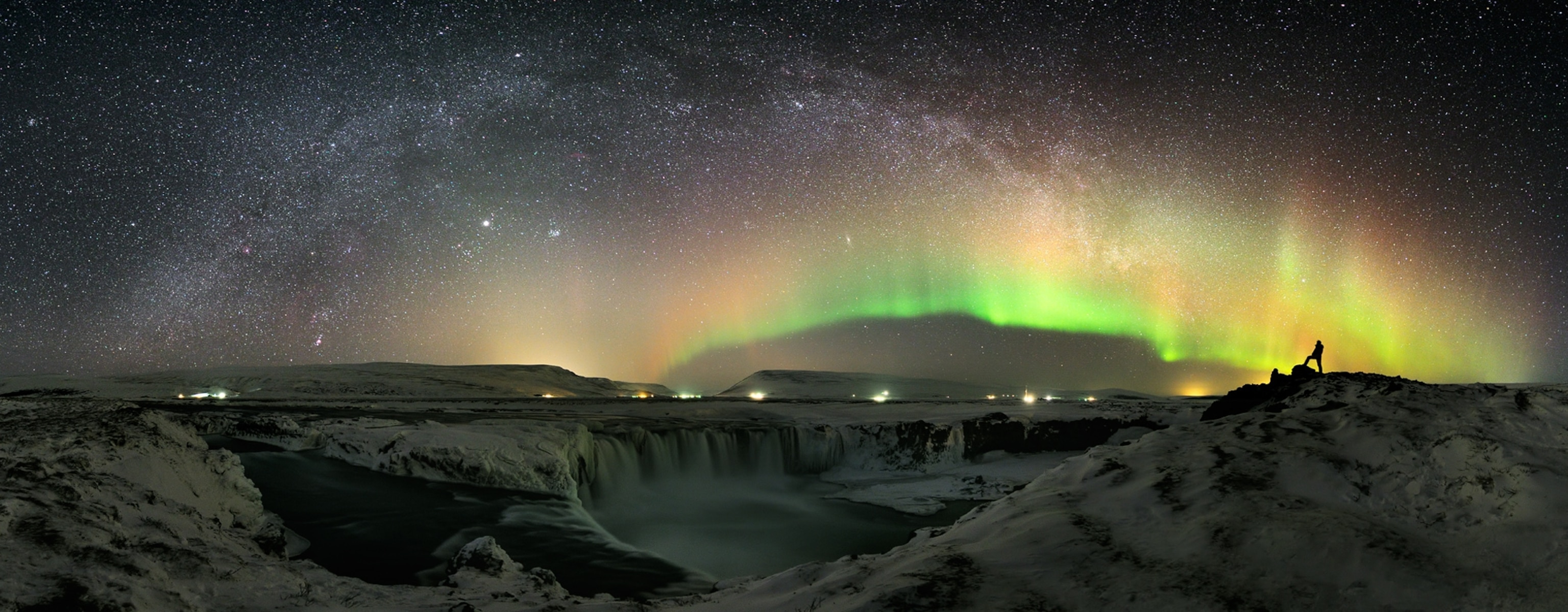 The World at Night - A panorama picture of the aurora borealis above a waterfall.