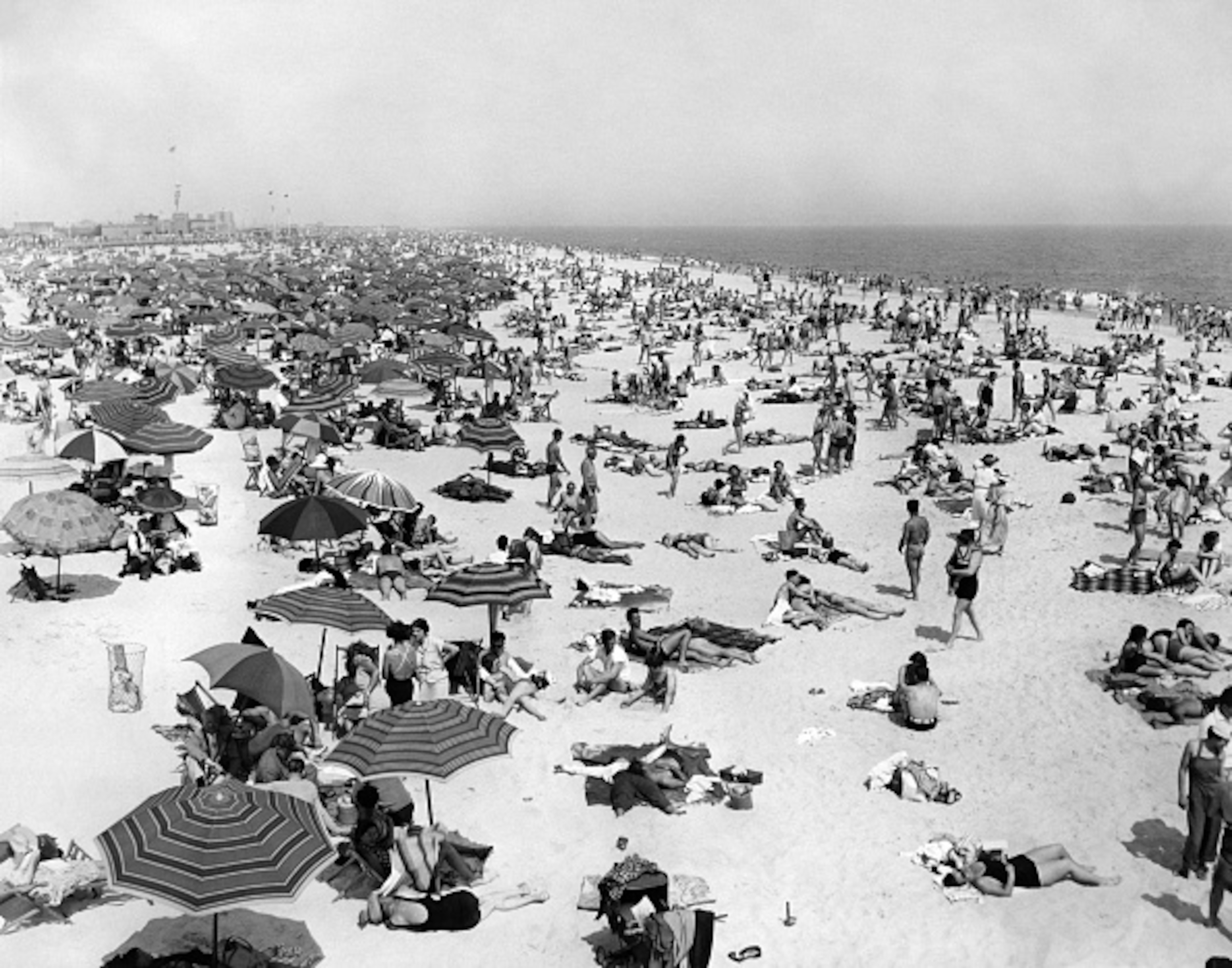 An archival photo from 1939, featuring people covering a beach, laying in the heat.