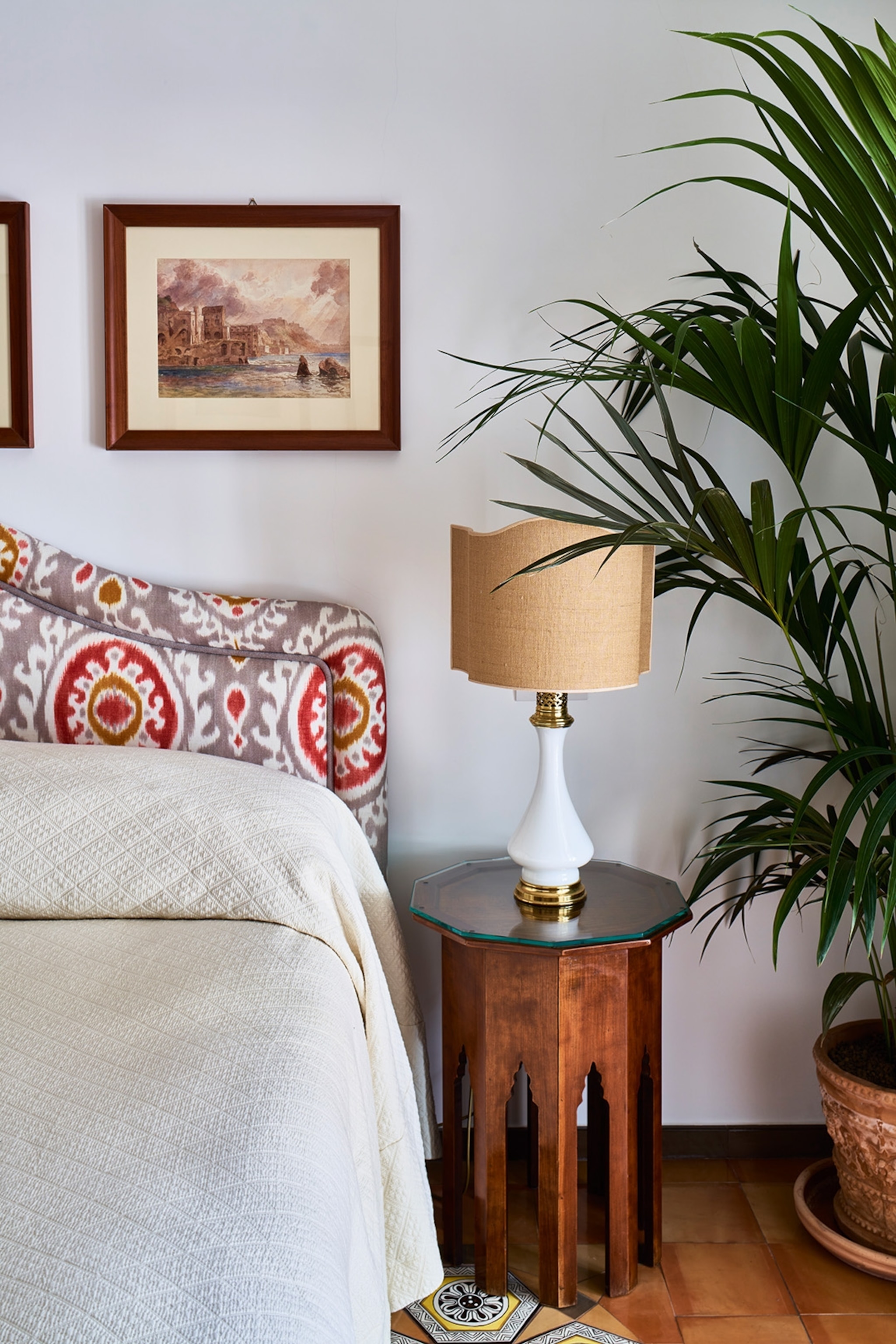 A bed with a bright headboard next to a beige lamp and large pot plant.