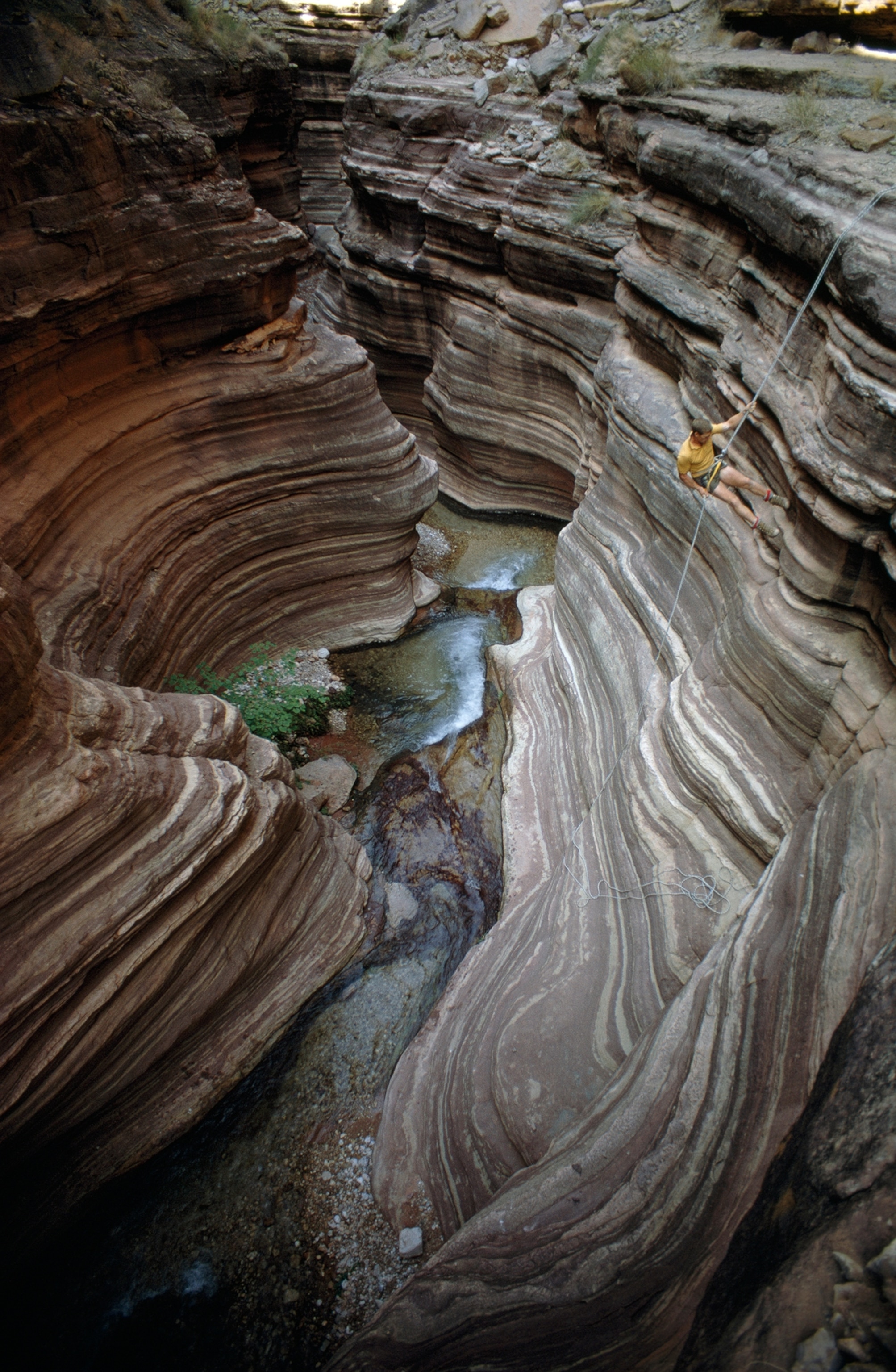 A man rappels down a sheer cliff above Deer Creek Falls.