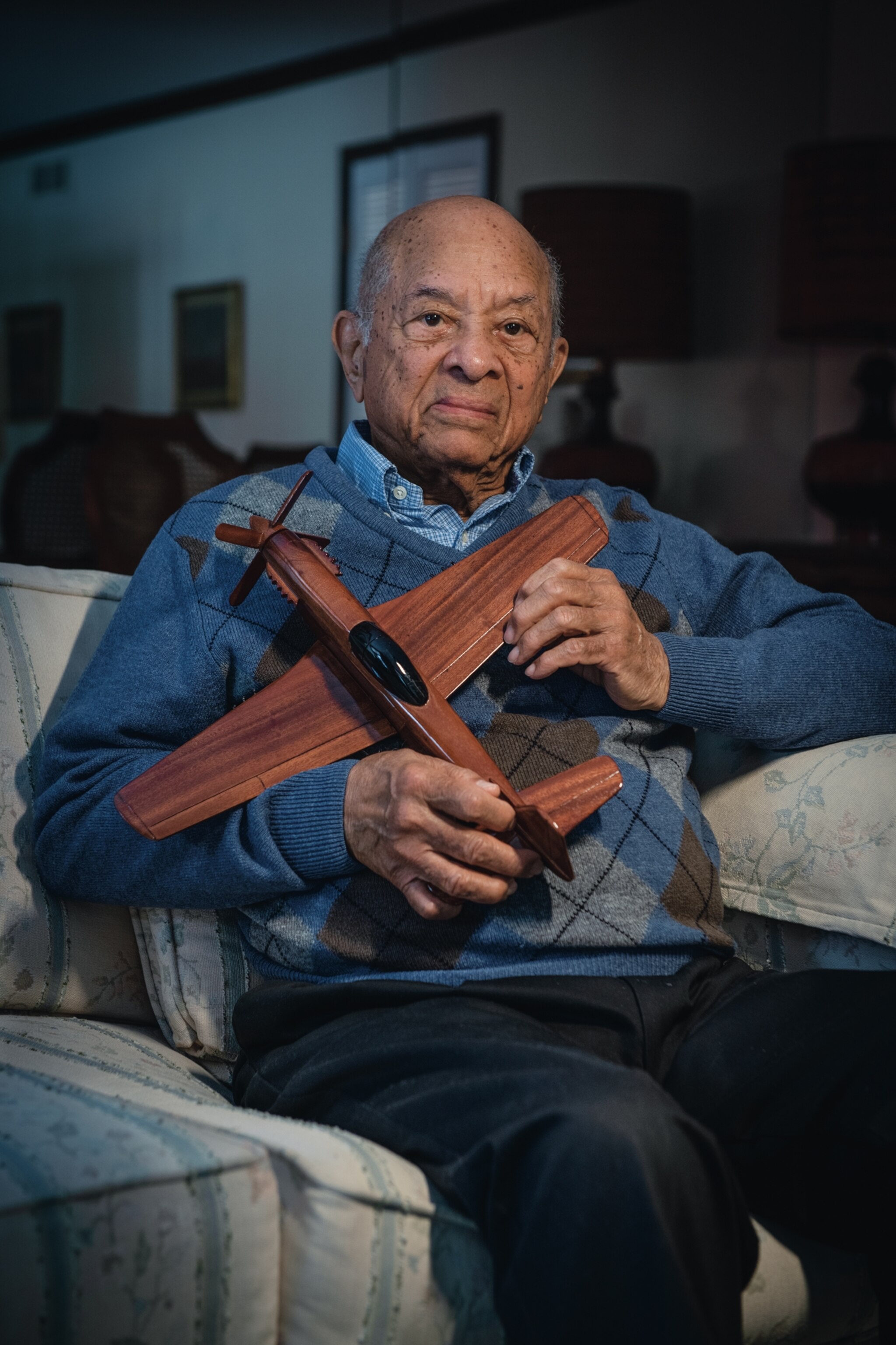 a man in a blue sweater holding a wooden airplane