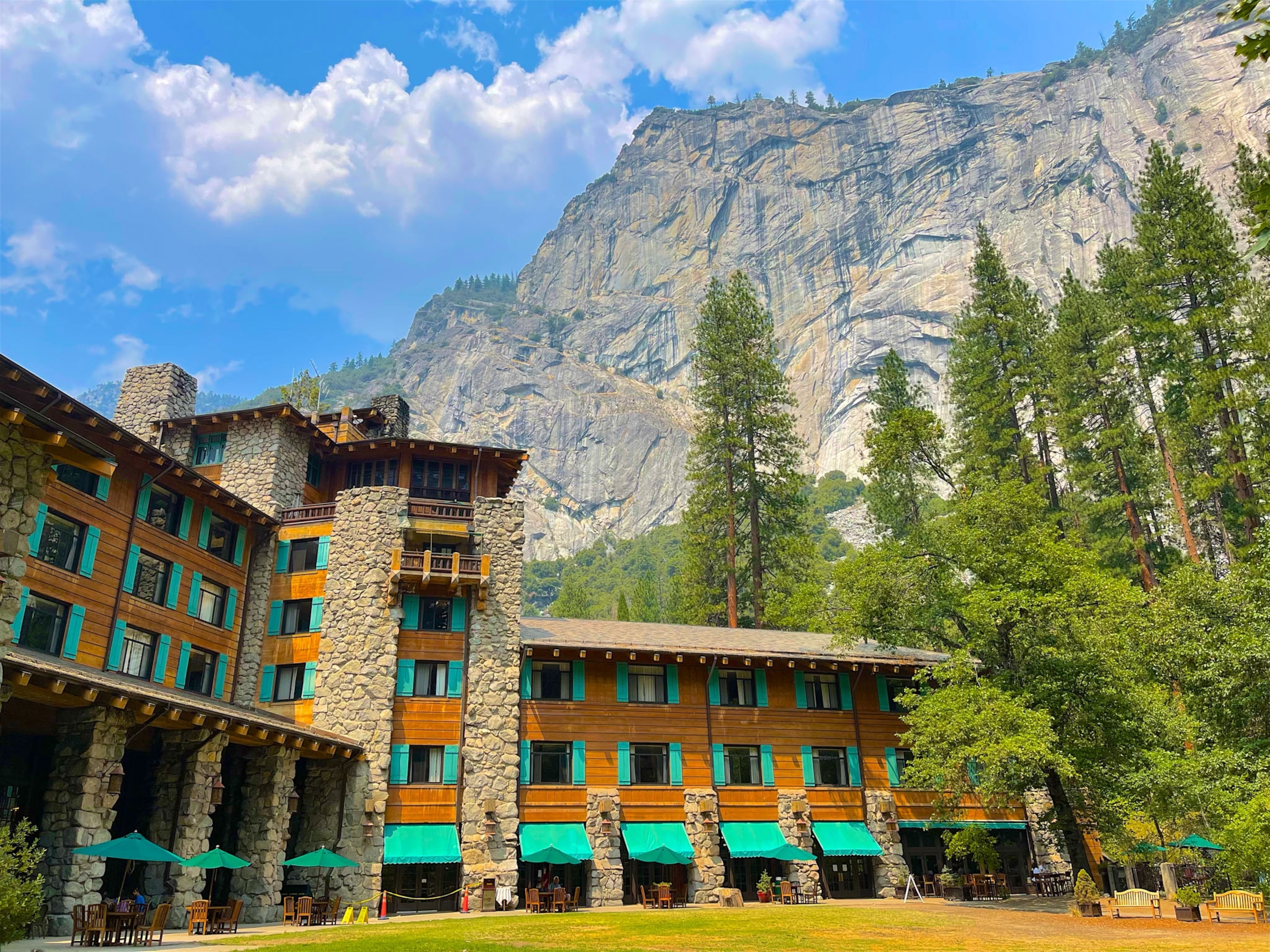 An exterior view of lodge hotel towered by a large cliffside mountain.