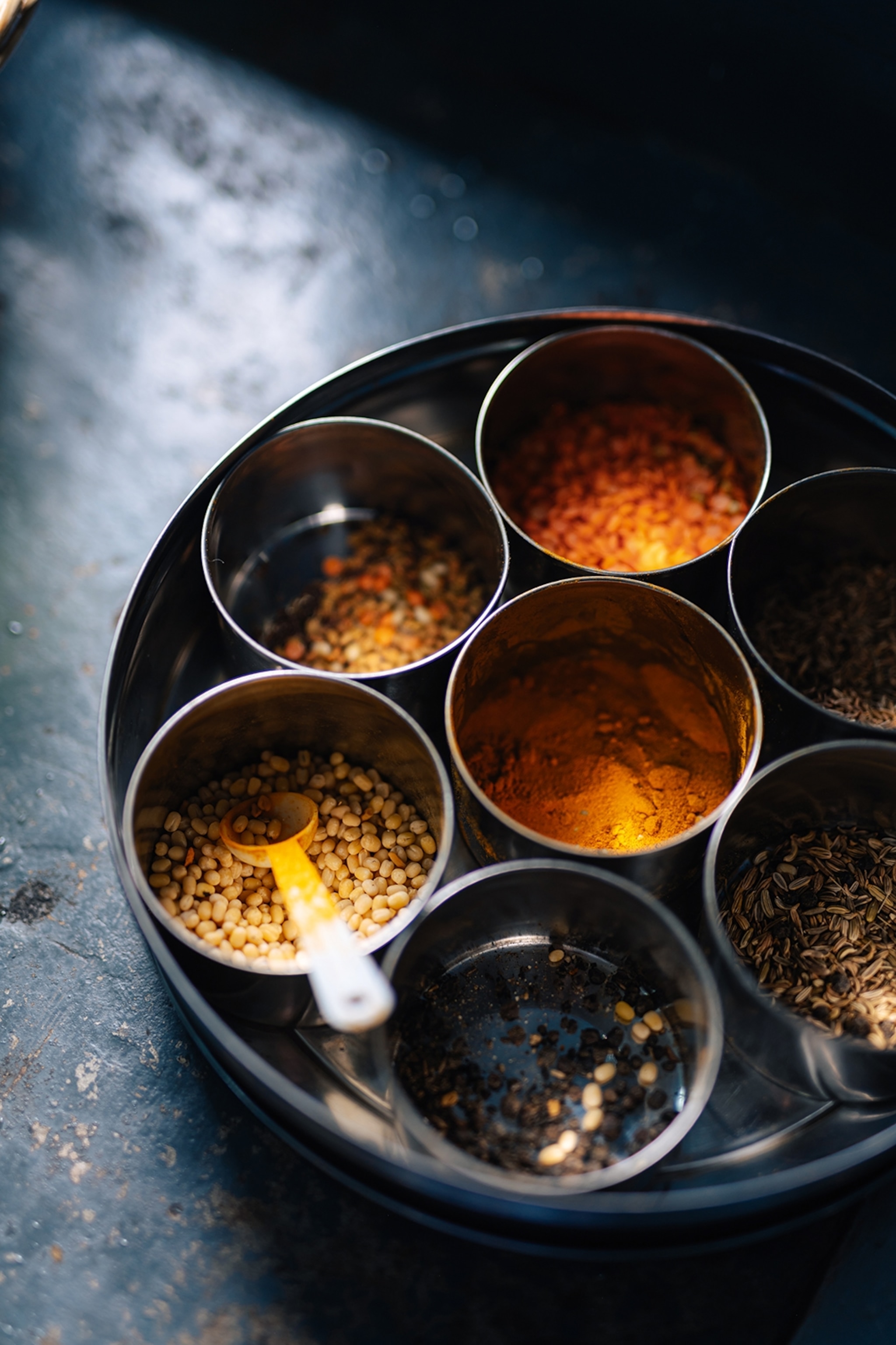 A close-up of a typically Indian lazy Susan with seven small tins containing different spices in a bigger round tin plate.