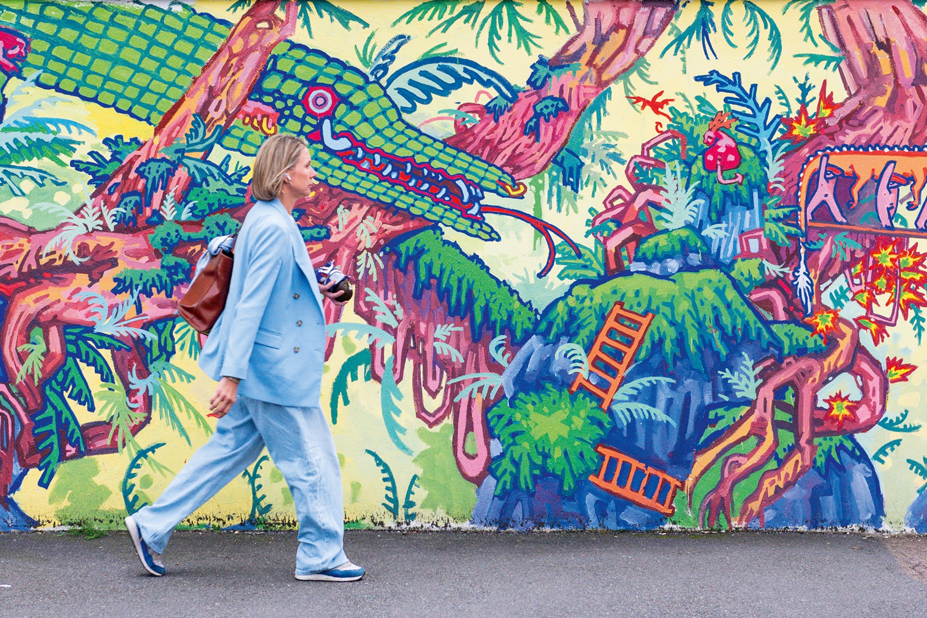 A woman walks in front of a mural wall.