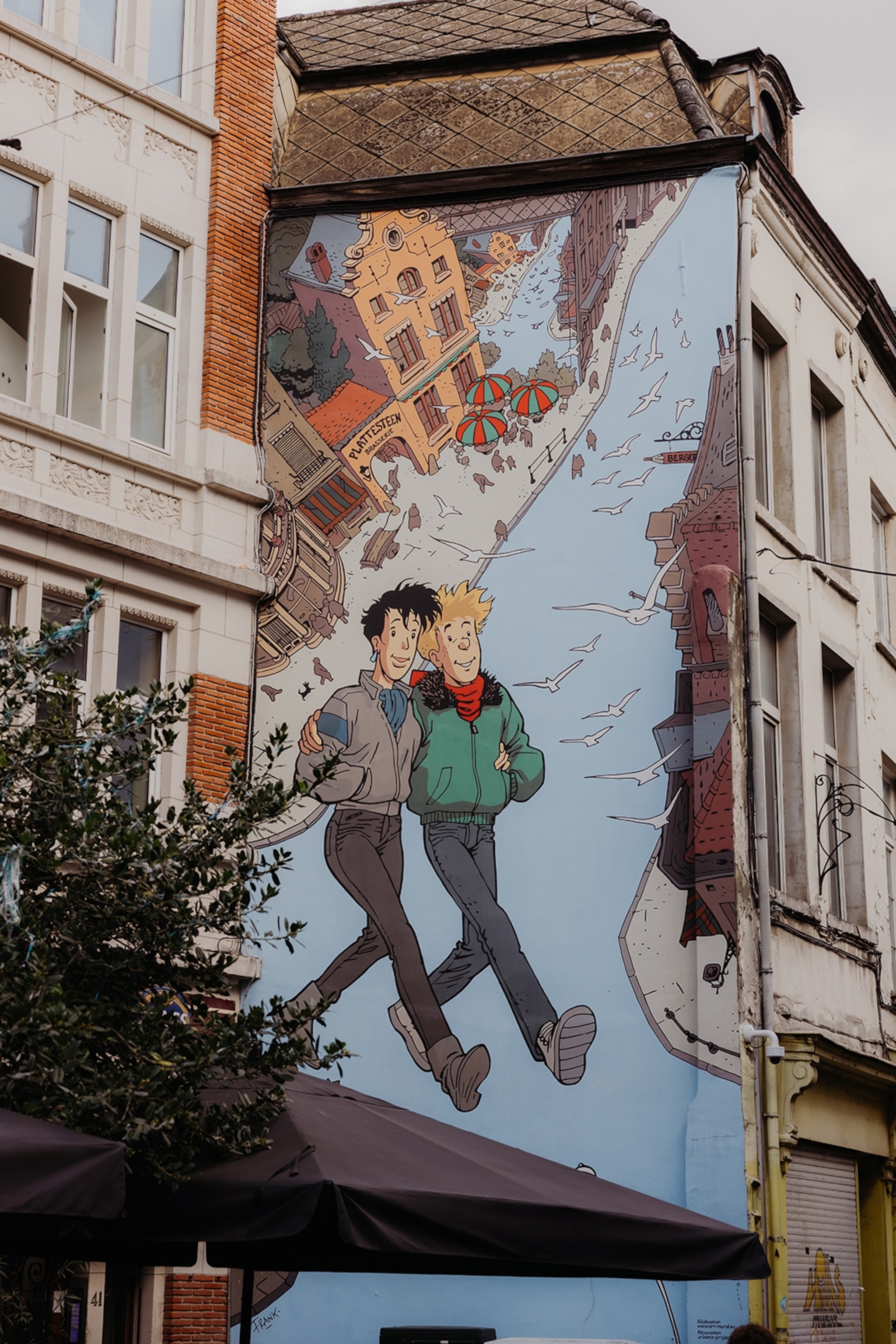 A close-up of a mural on the side of a residential building, depicting two comic characters walking in the air together above a city river.